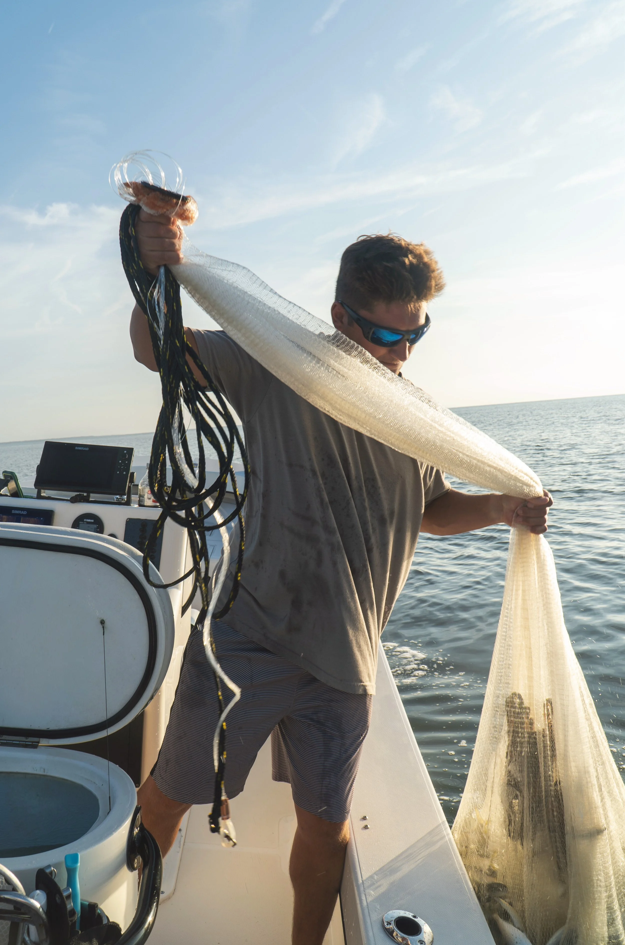 Man on a boat handling a fishing net in the open water during daylight.