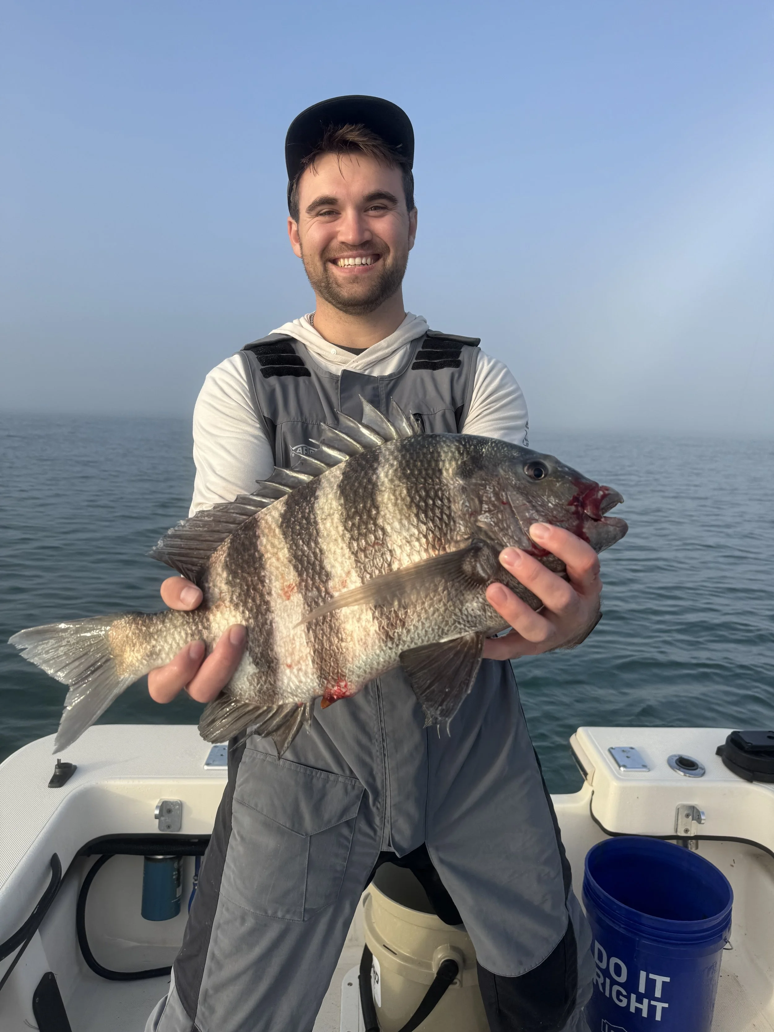 A man smiling on a boat holding a large fish caught while fishing at sea.