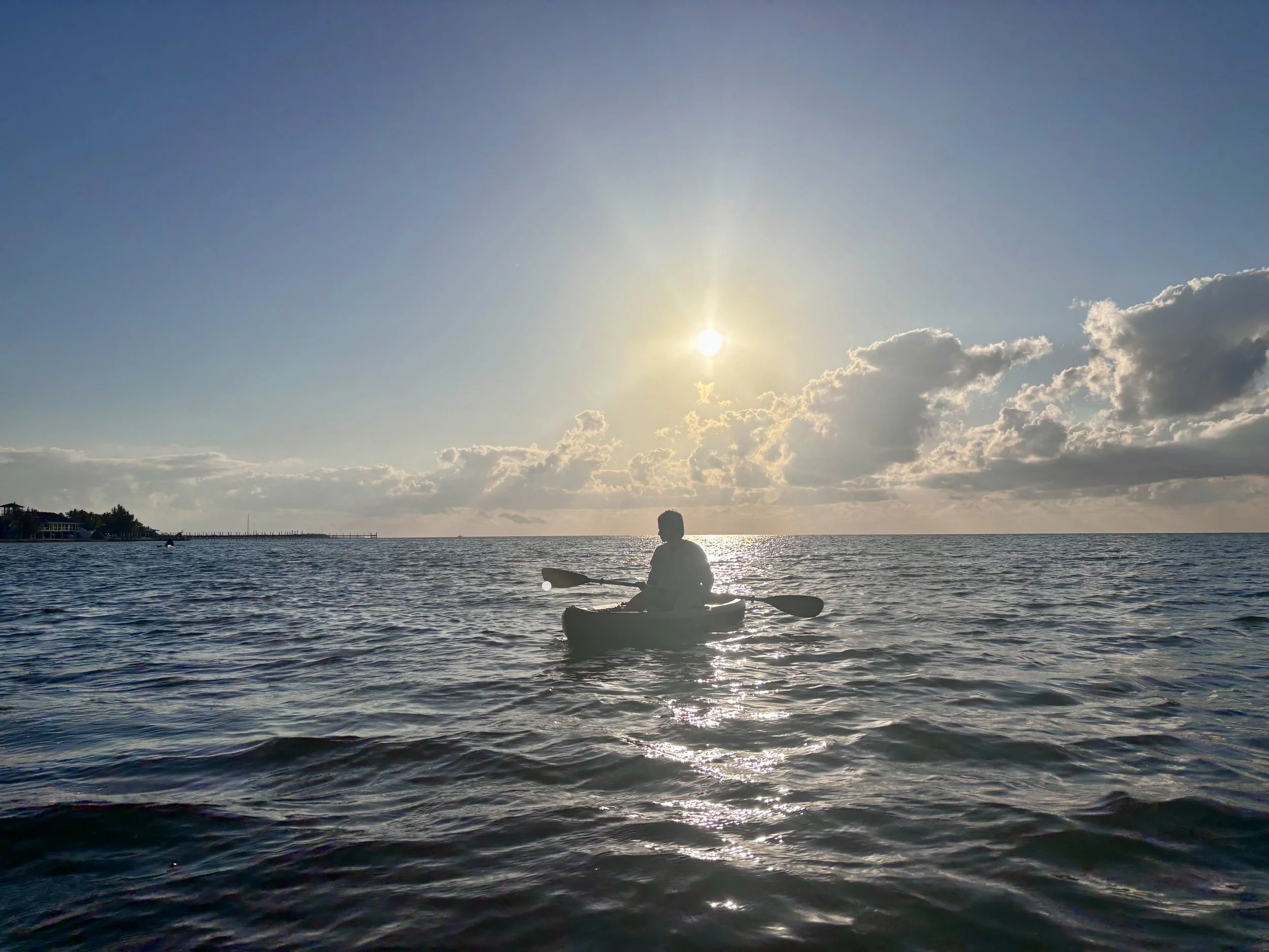 A person kayaking on the water during sunset with a partly cloudy sky.