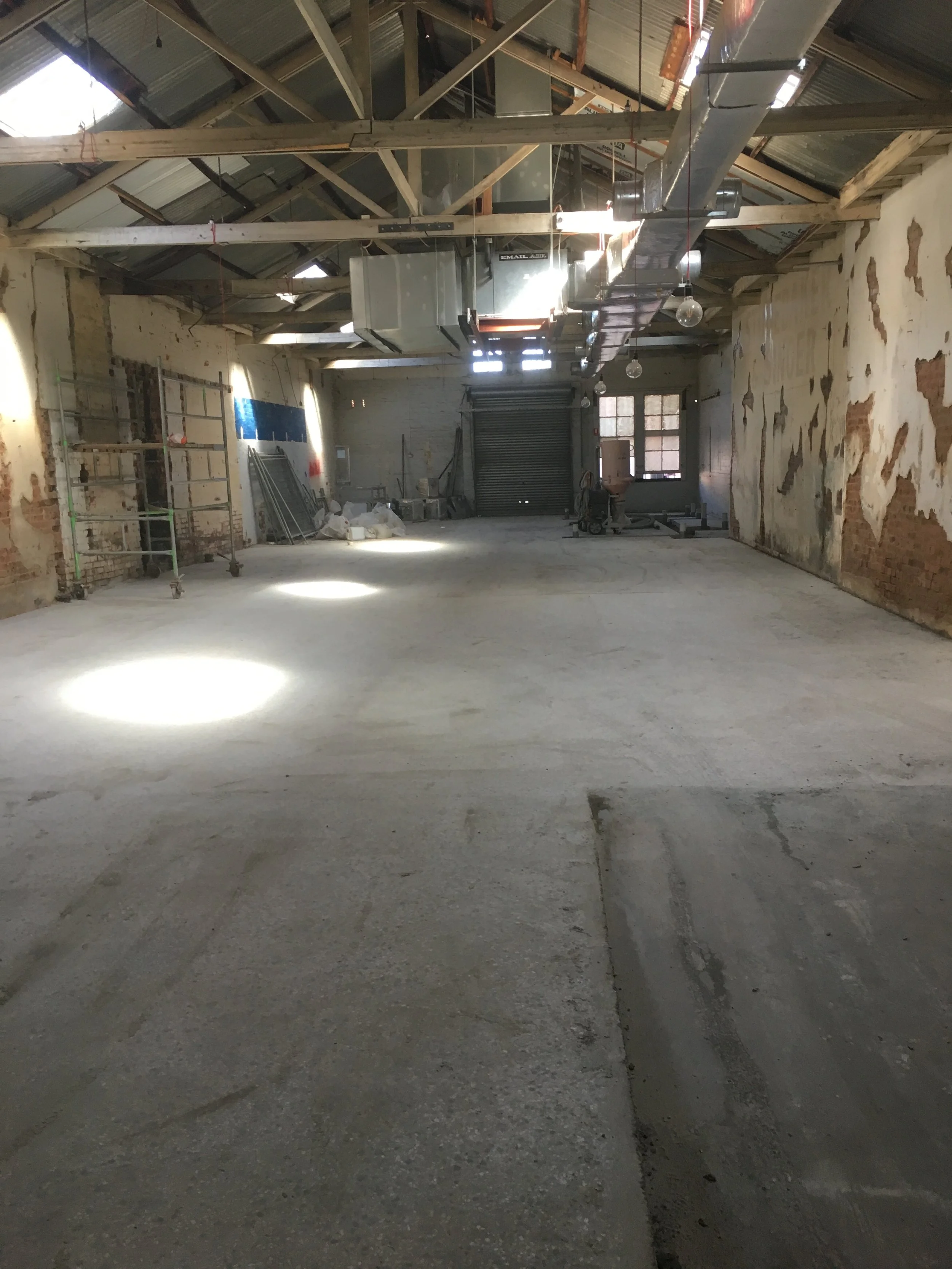 unfinished interior of a building under construction with exposed wooden beams, ductwork, scaffolding, and construction materials on the floor.