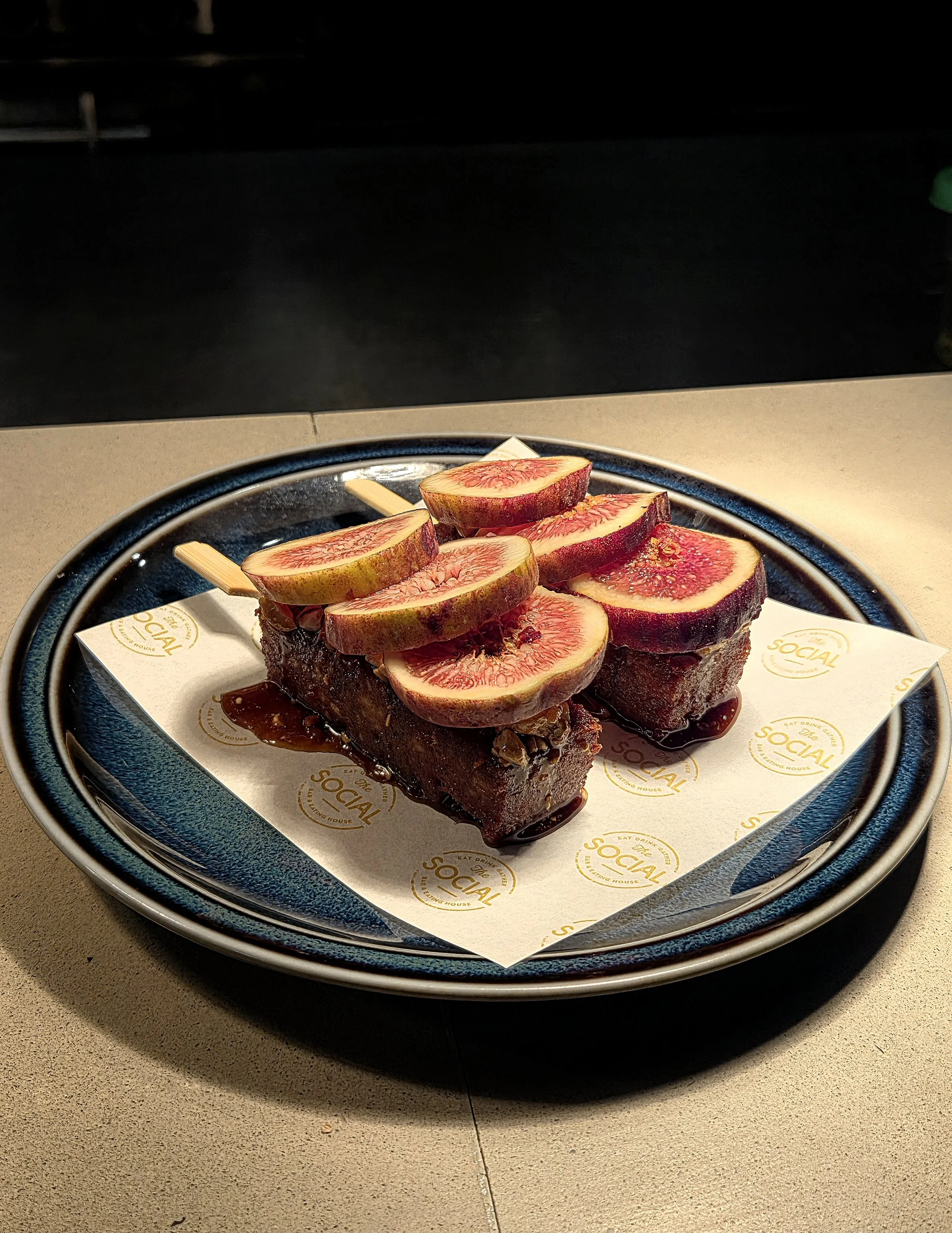 Slices of fig on top of a chocolate cake with sauce drizzled around it on a black plate.