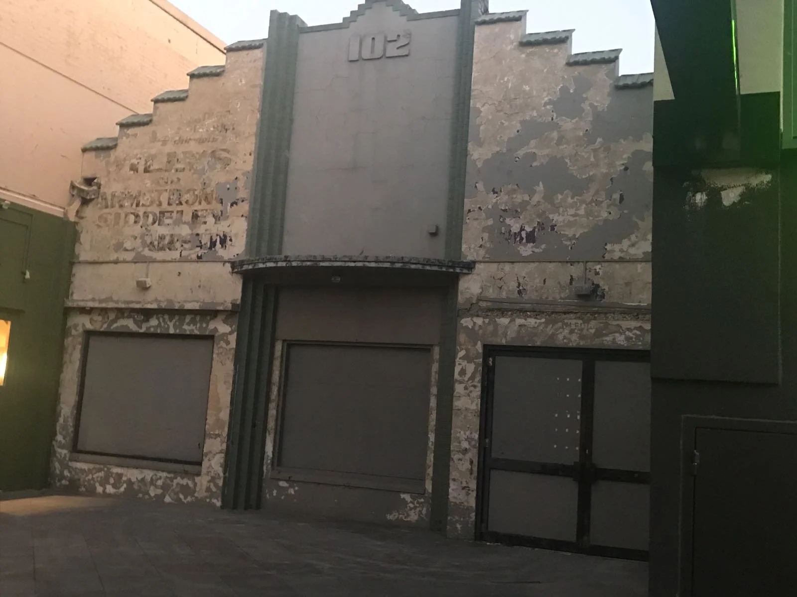 An old, weathered building with peeling paint and boarded-up windows. The building has a protruding vertical sign with the number '102' at the top. The facade appears neglected and abandoned.