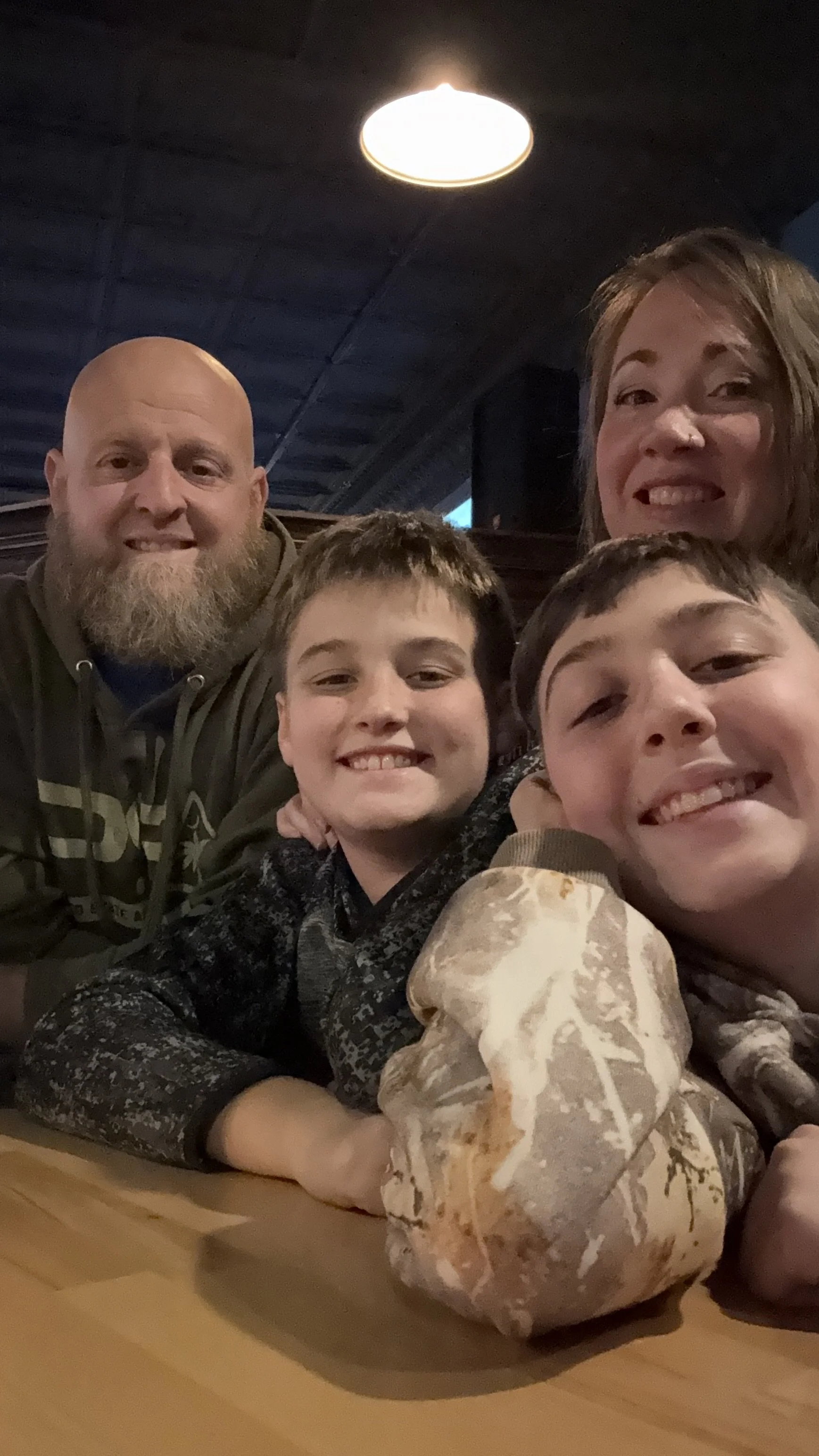 Group of four people, two adults and two children, smiling and taking a selfie at a restaurant, with a large decorative stone on the table.