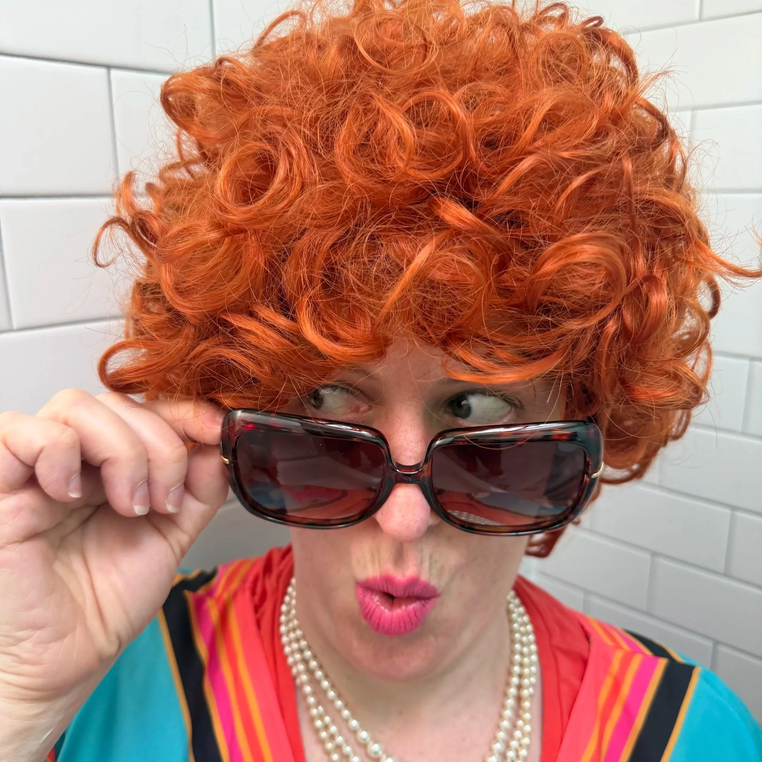 Mrs. Roper Romp costume with patterned caftan, curly red wig, and big sunglasses.