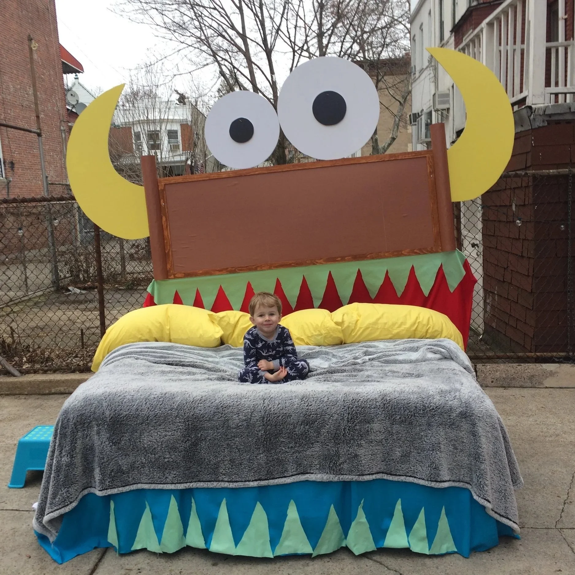 Small boy sitting on giant bed designed as monster, with googly eyes, horns, and mouth