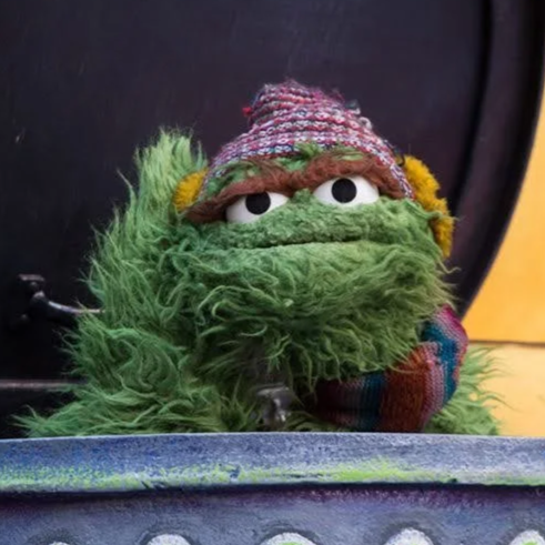 Oscar the Grouch puppet in trash can wearing winter hat and scarf on Sesame Street float at Macy's Thanksgiving Parade.