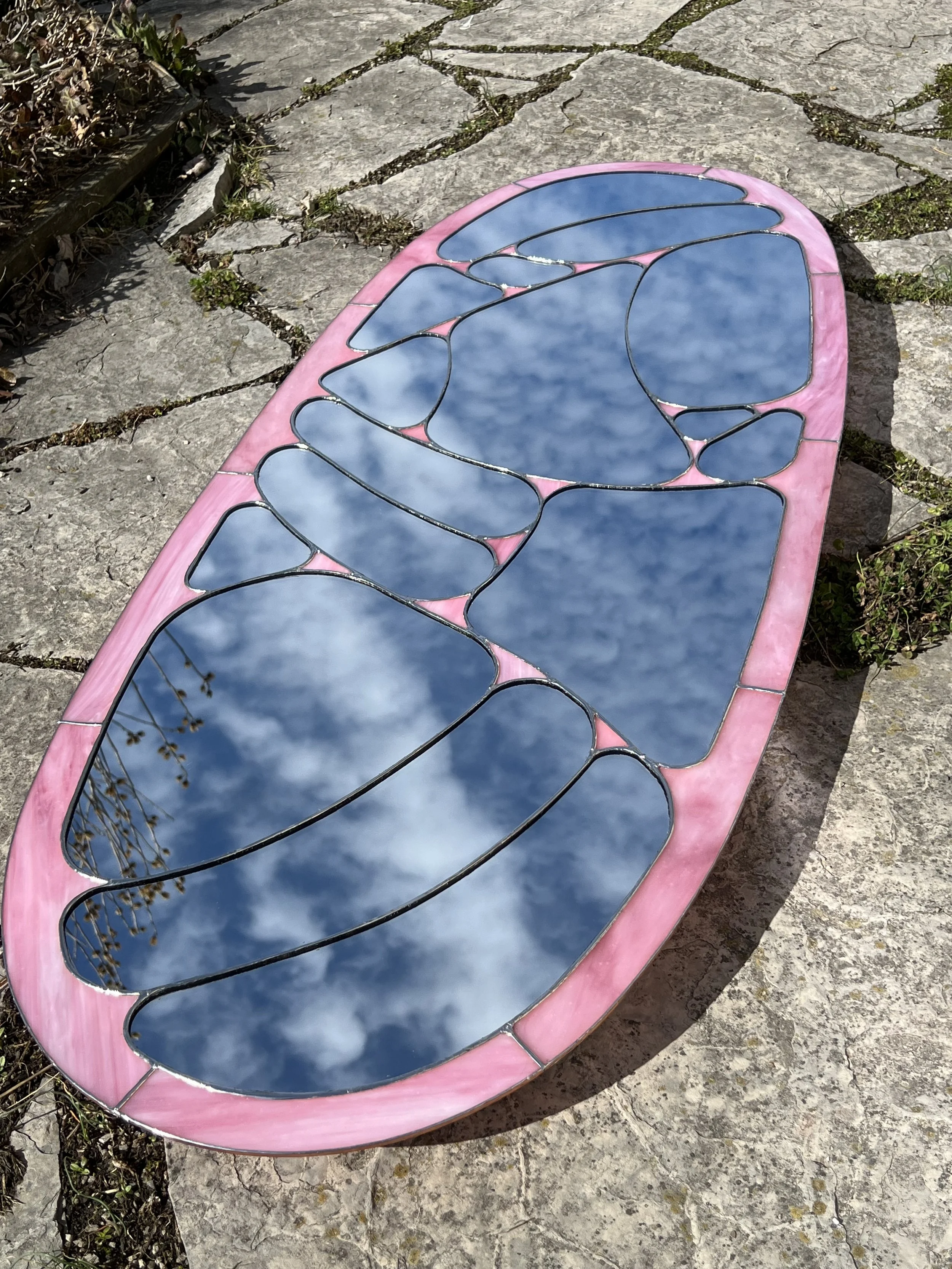 a pink mirror which resembles a flower like design, hand made, one of a kind art, made of pink stained glass