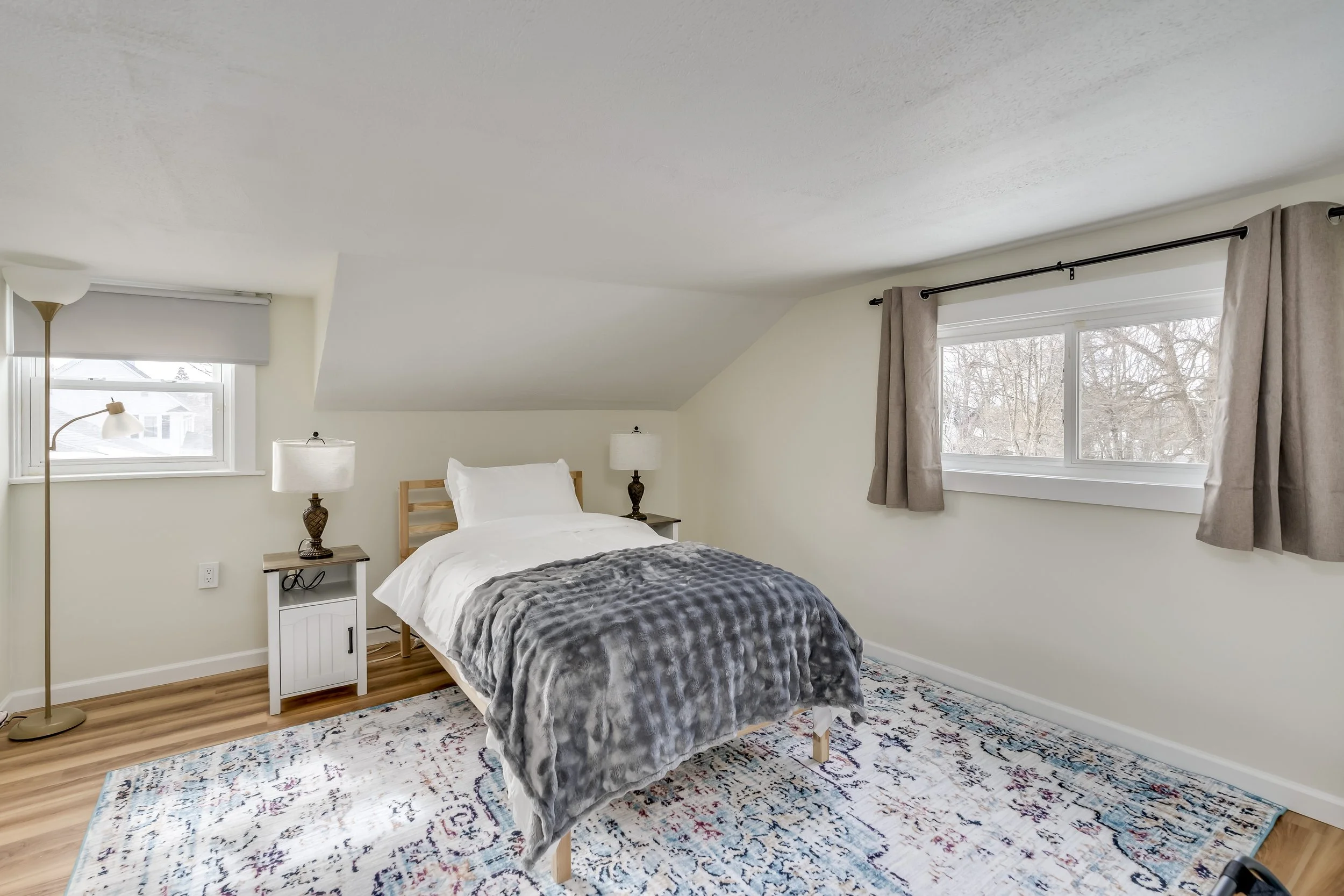 Bedroom with a bed, two nightstands with lamps, a window with curtains, and a patterned rug.