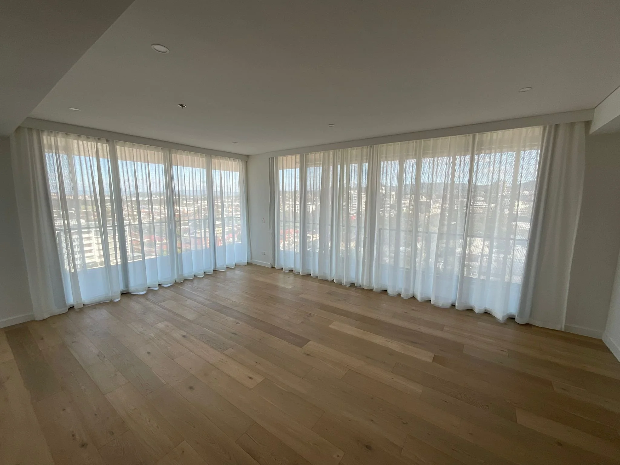 Room with large floor-to-ceiling windows with white curtains and wooden flooring