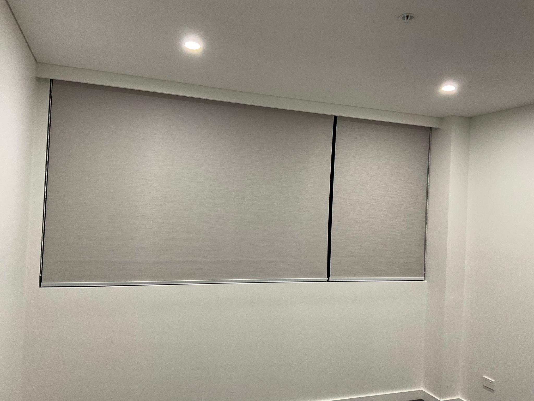 An interior view of a closed sliding door with a metallic frame, set within a white wall, and a ceiling with two recessed lights.