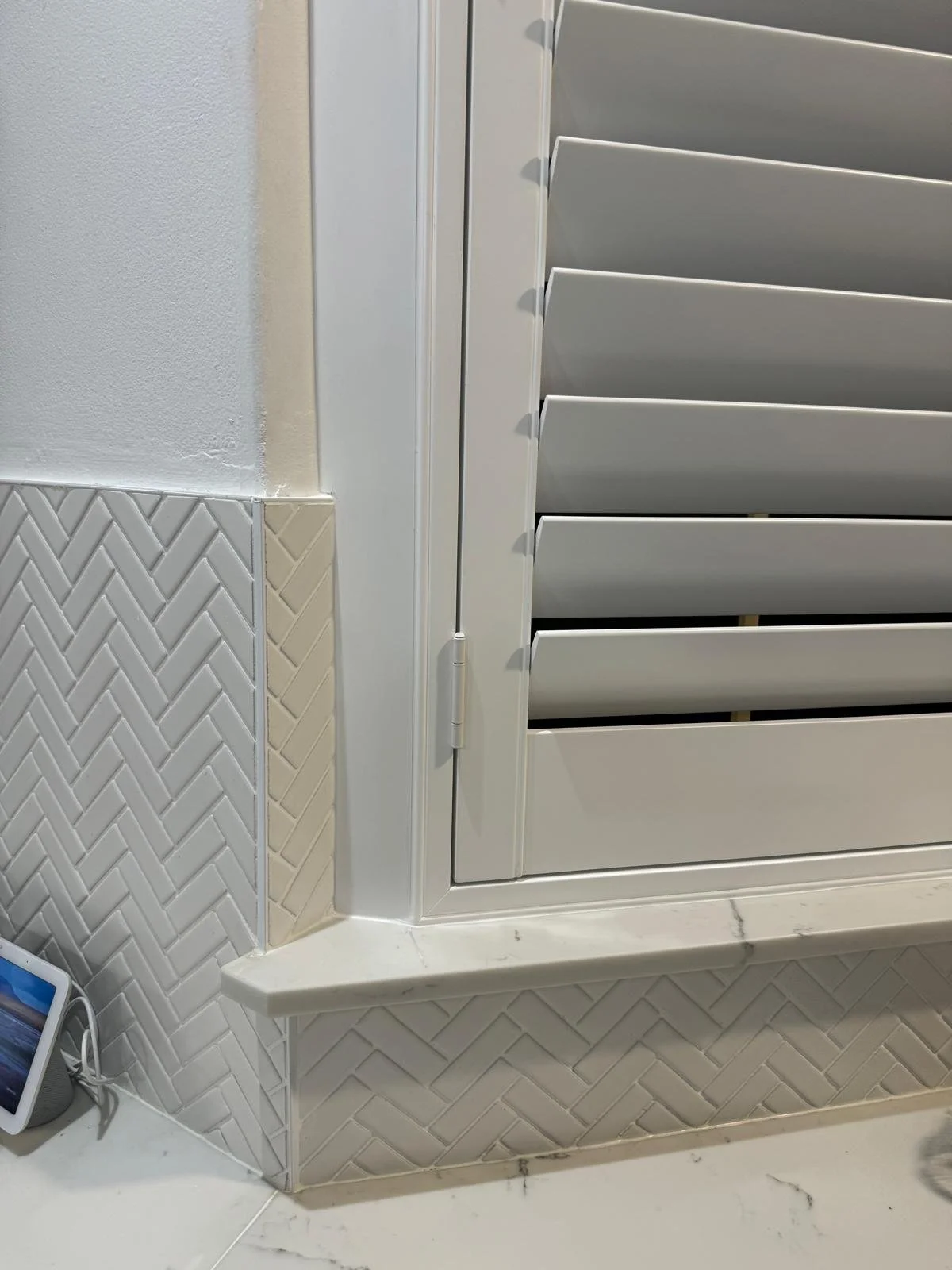 Close-up of a white indoor air vent or shutter mounted on a wall with beige corner tiles and a white marble countertop.