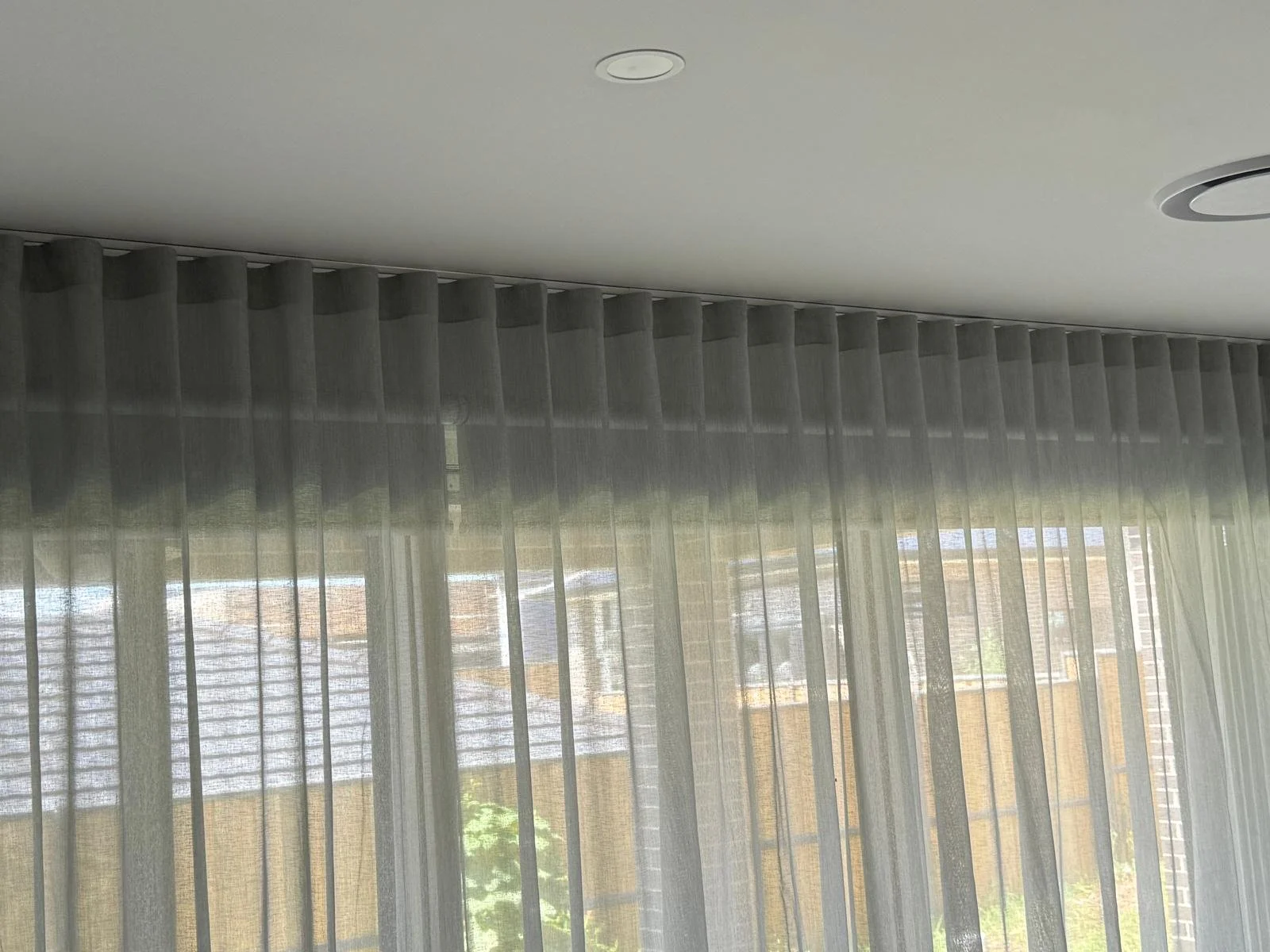 Interior view of a room with sheer curtains hanging in front of large windows and a white ceiling with recessed lighting.
