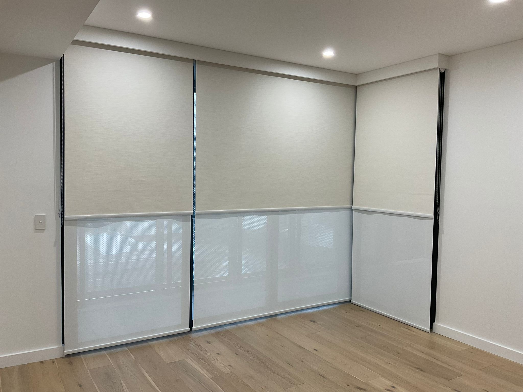 A room with a wardrobe featuring sliding doors, one with opaque glass and the other with a faint pattern, set against white walls and ceiling with ceiling lights, and hardwood flooring.