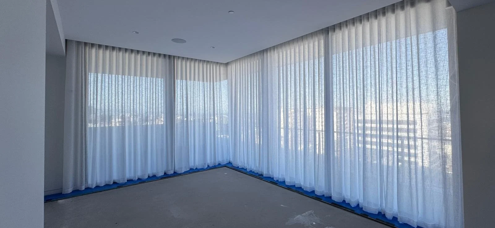 Empty room with large windows covered by sheer white curtains, letting in natural light.
