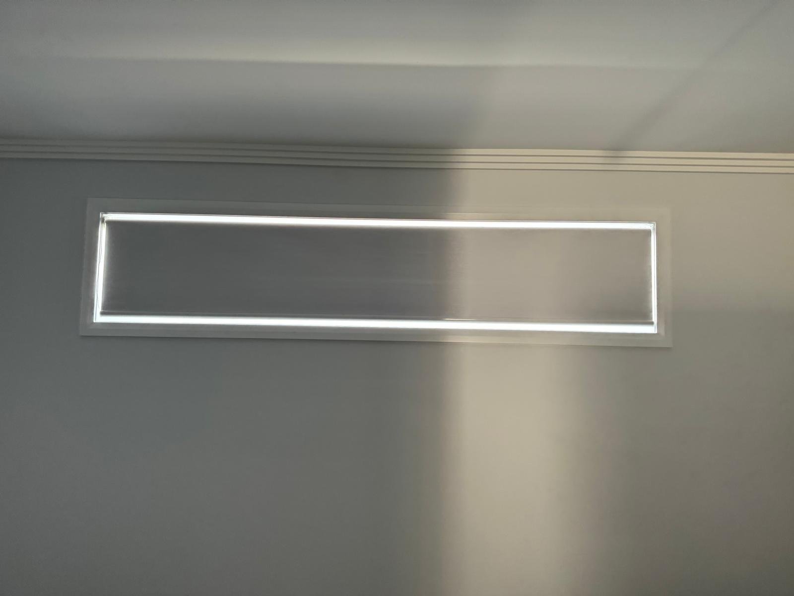 A rectangular window or vent on a light gray wall, with sunlight casting a shadow on the right side.