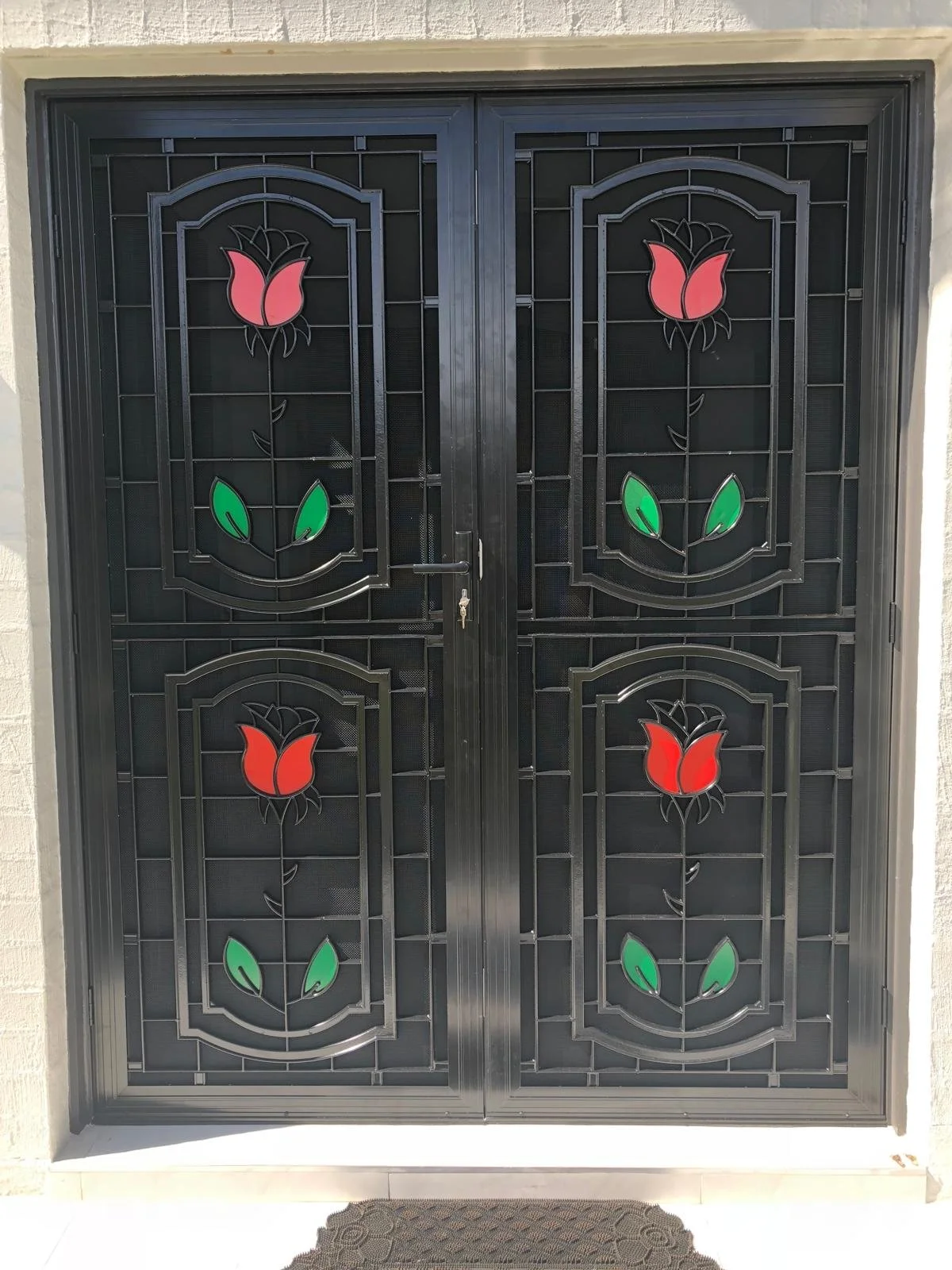 Black metal gate with stained glass floral design featuring pink and red flowers with green leaves.