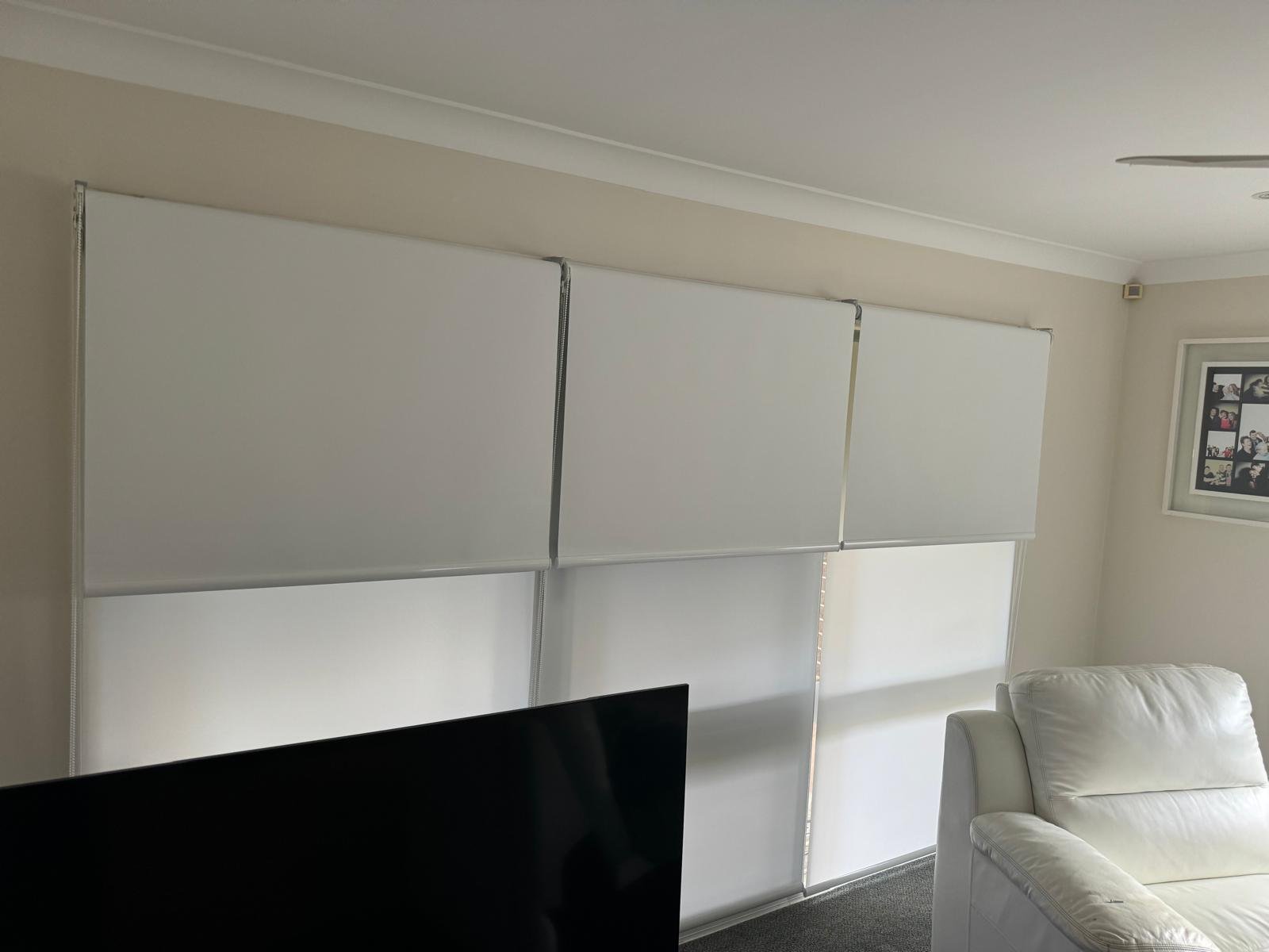 Living room with white window blinds, a white couch, and a picture frame on the wall.