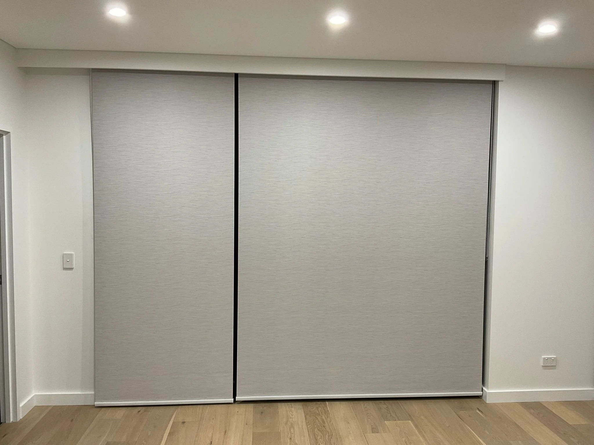 A closed, light gray sliding closet door in a white-walled room with a wooden floor and round ceiling lights.