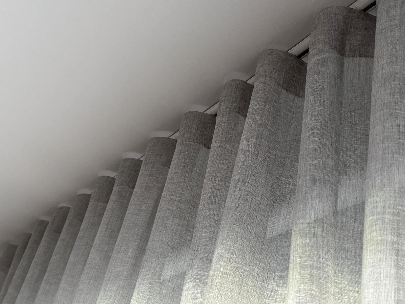 Close-up image of a light gray fabric curtain with vertical pleats hanging from a curtain rail.