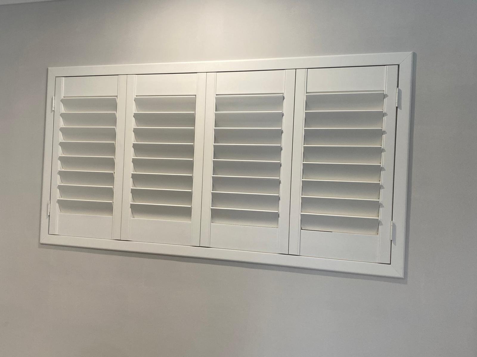 White plantation shutters mounted on a white wall.