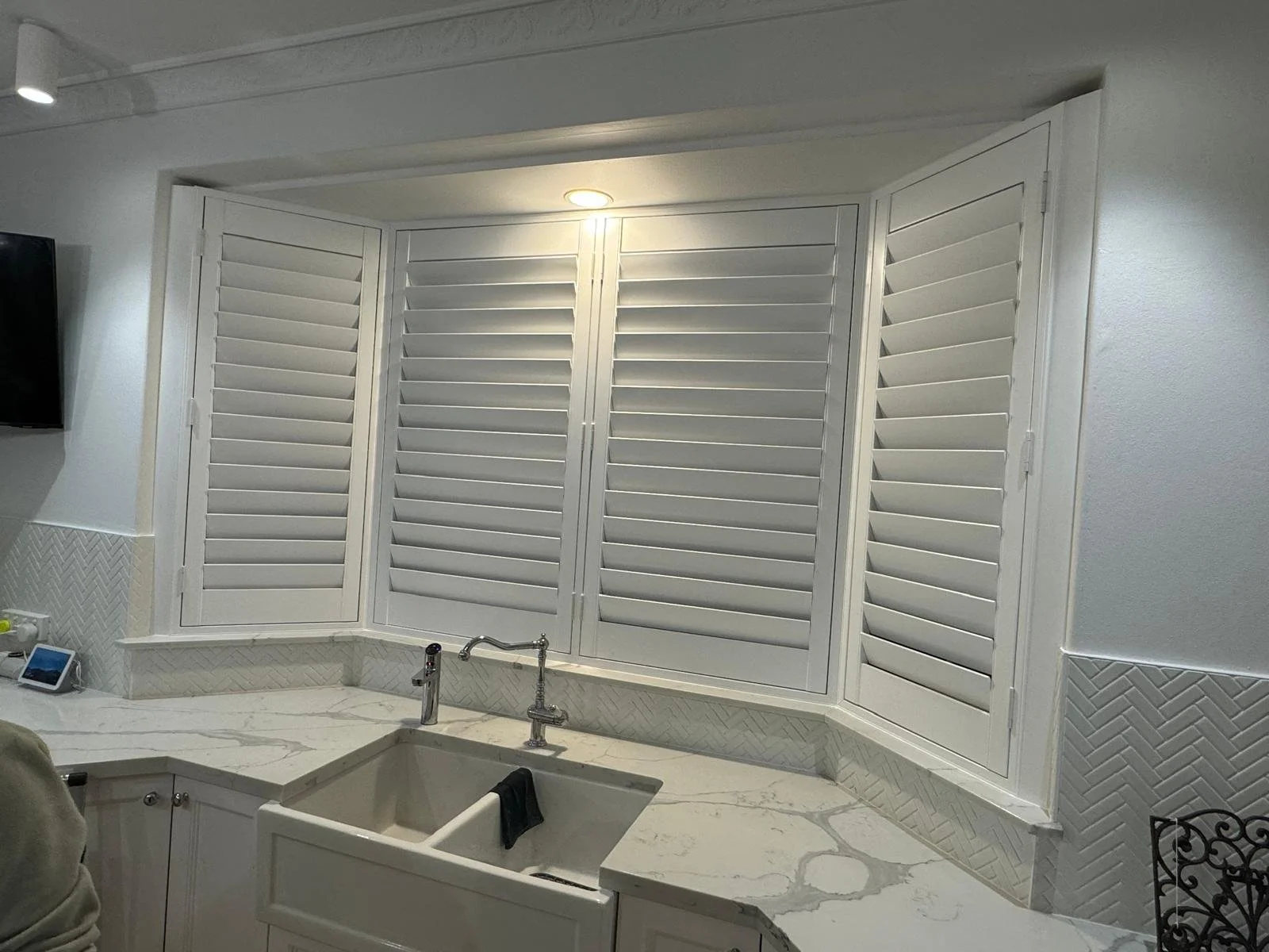 Kitchen with white cabinets, marble countertop, a farmhouse sink, and white plantation shutters covering a window.