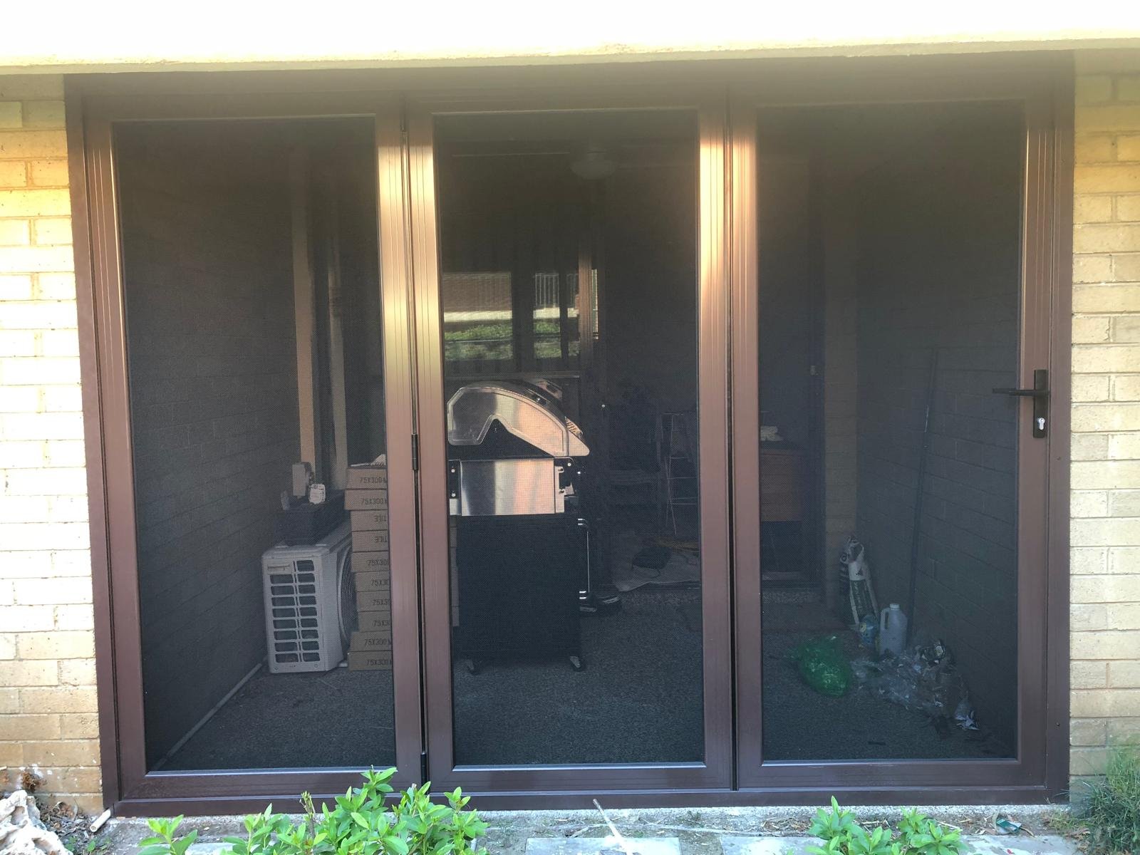 Sliding glass door with a barbecue grill and miscellaneous items inside, including boxes and cleaning supplies.