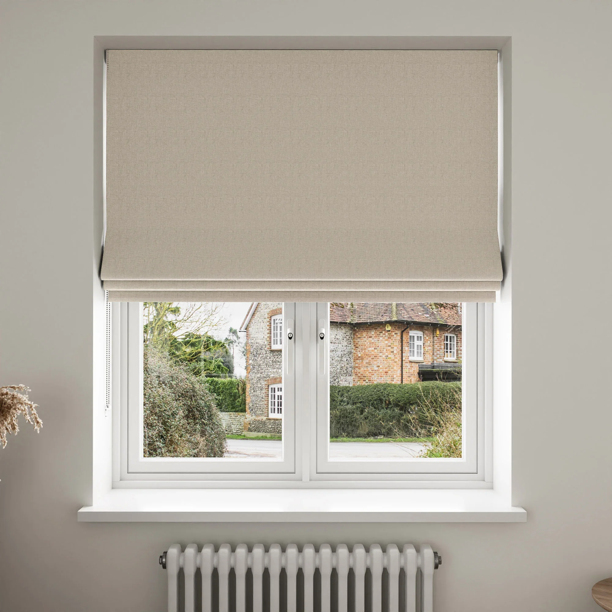 White window with a beige roller blind partially exposed, view of a house with brick walls, trees, and a grassy lawn outside.
