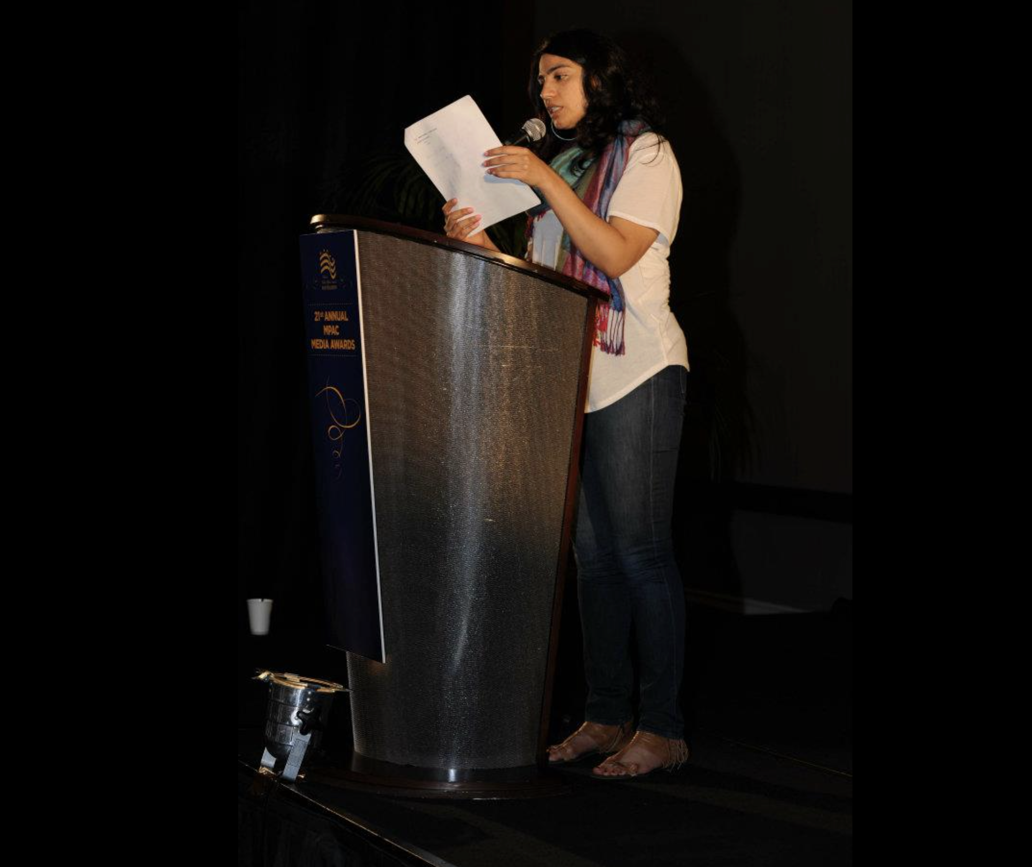 A woman standing at a podium, reading from papers, speaking into a microphone at an award event.