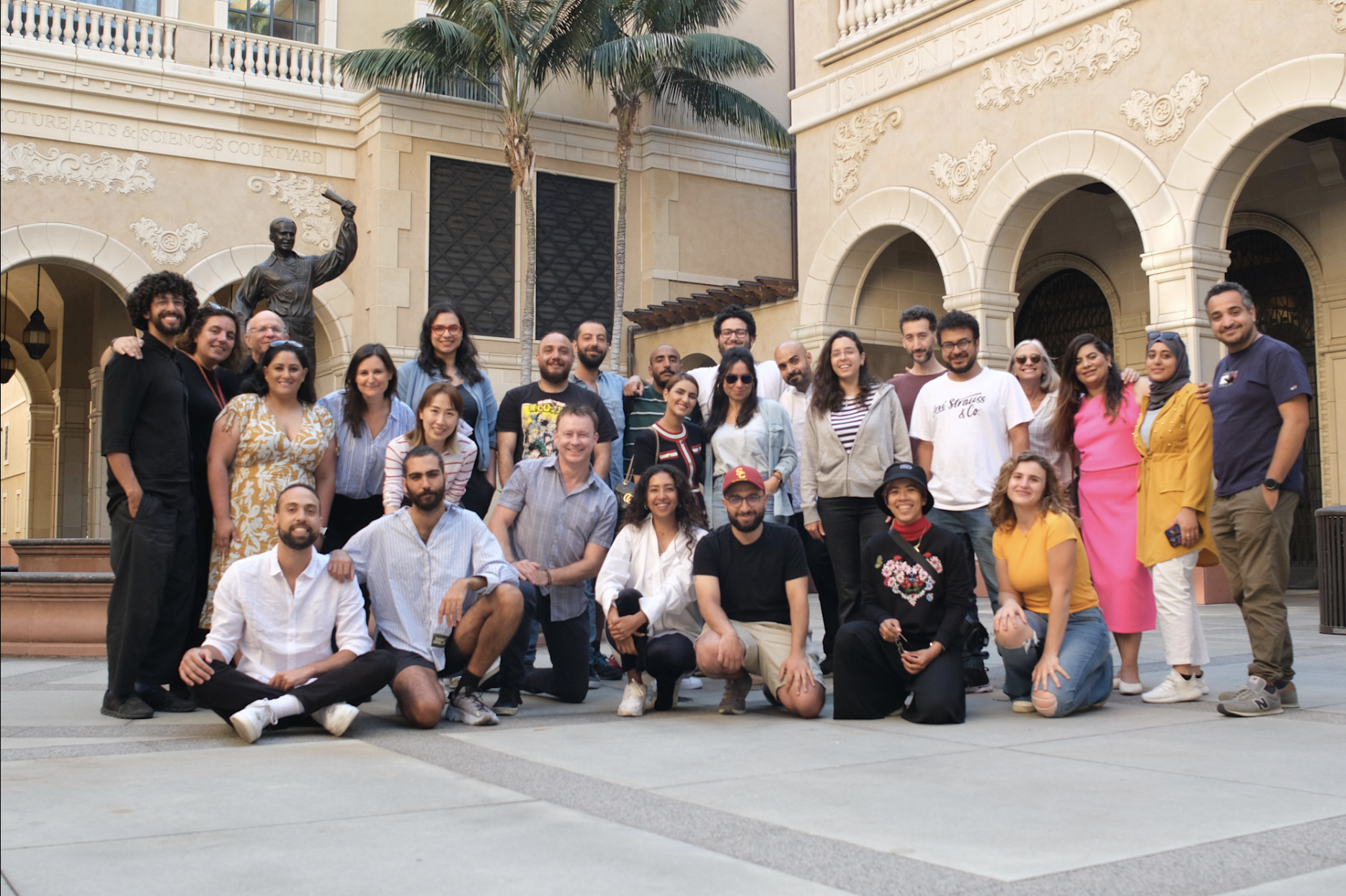 Group of diverse people posing together in an outdoor courtyard with a historic building and a statue behind them.