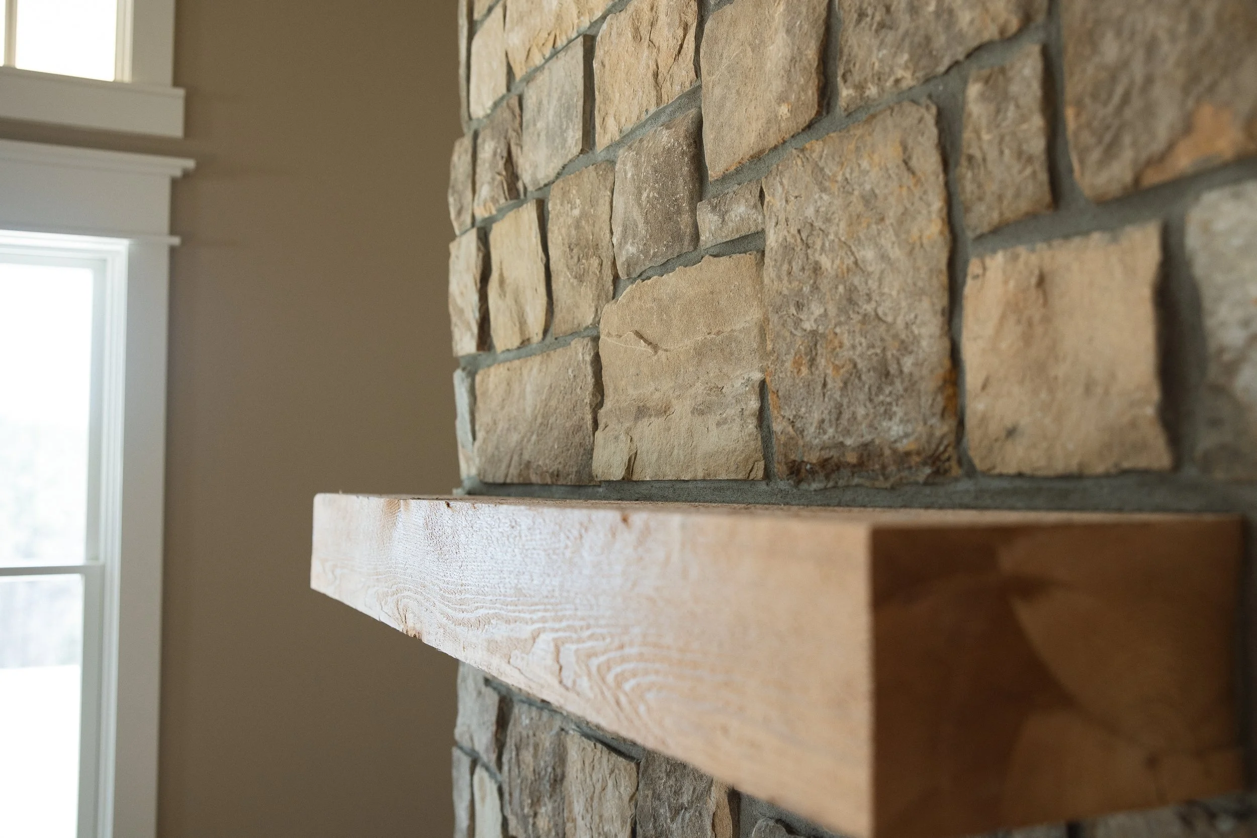 Close-up of a brick fireplace with a wooden mantel in a room with a window.