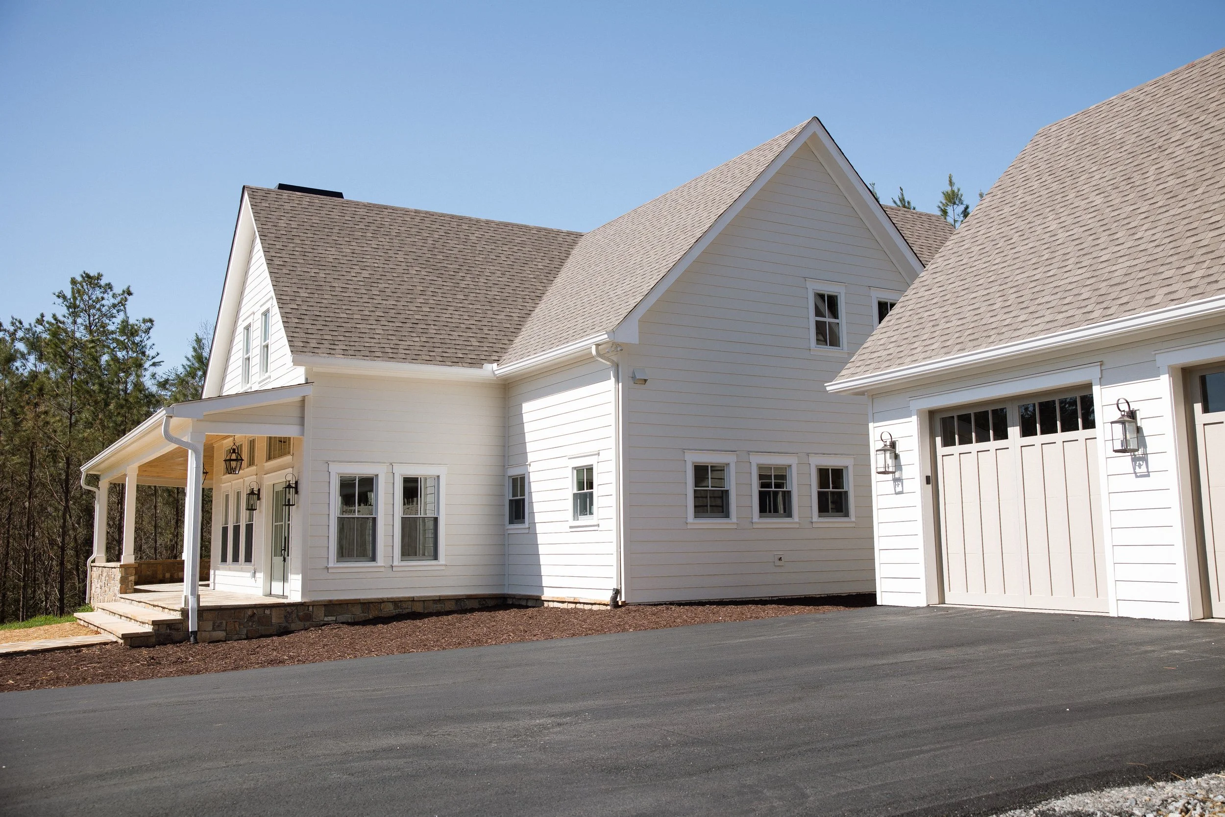 A modern white house with a garage, a front porch with steps, and multiple windows under a blue sky.