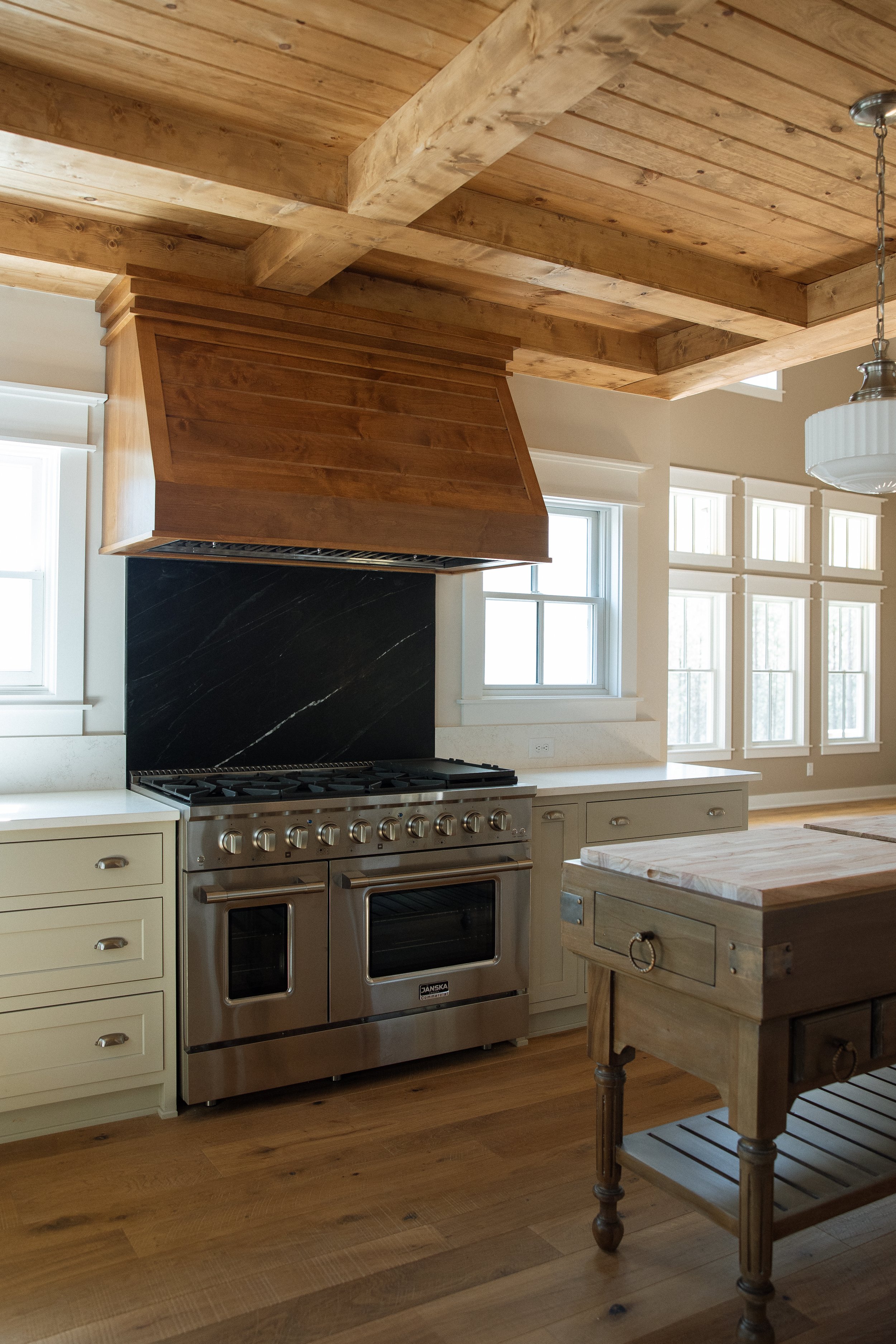 Kitchen with a stainless steel stove, black backsplash, cream cabinetry, wooden ceiling beams, and a wooden kitchen island.