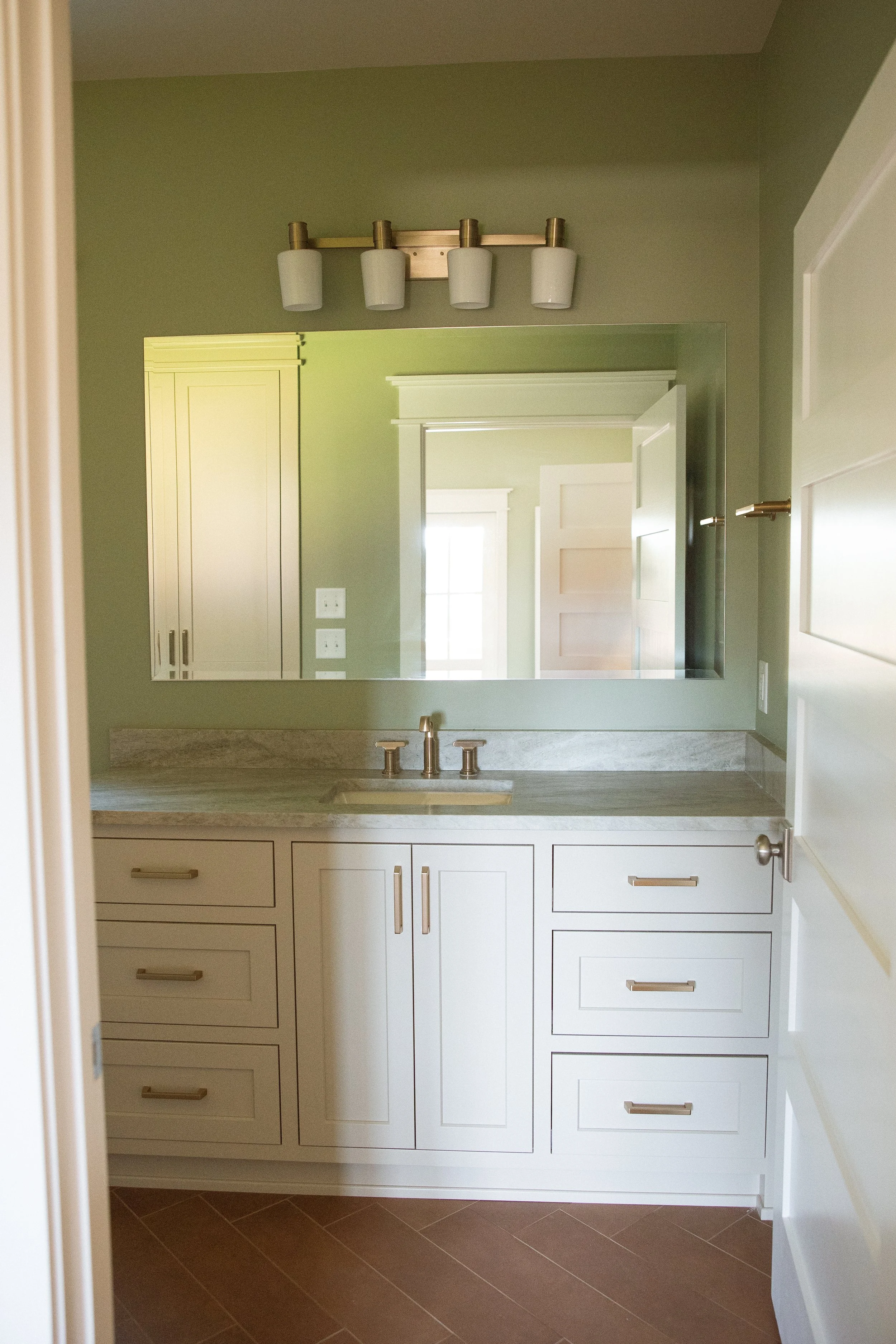 A bathroom vanity with a marble countertop, a rectangular mirror, and a modern light fixture with four cylindrical lights above.
