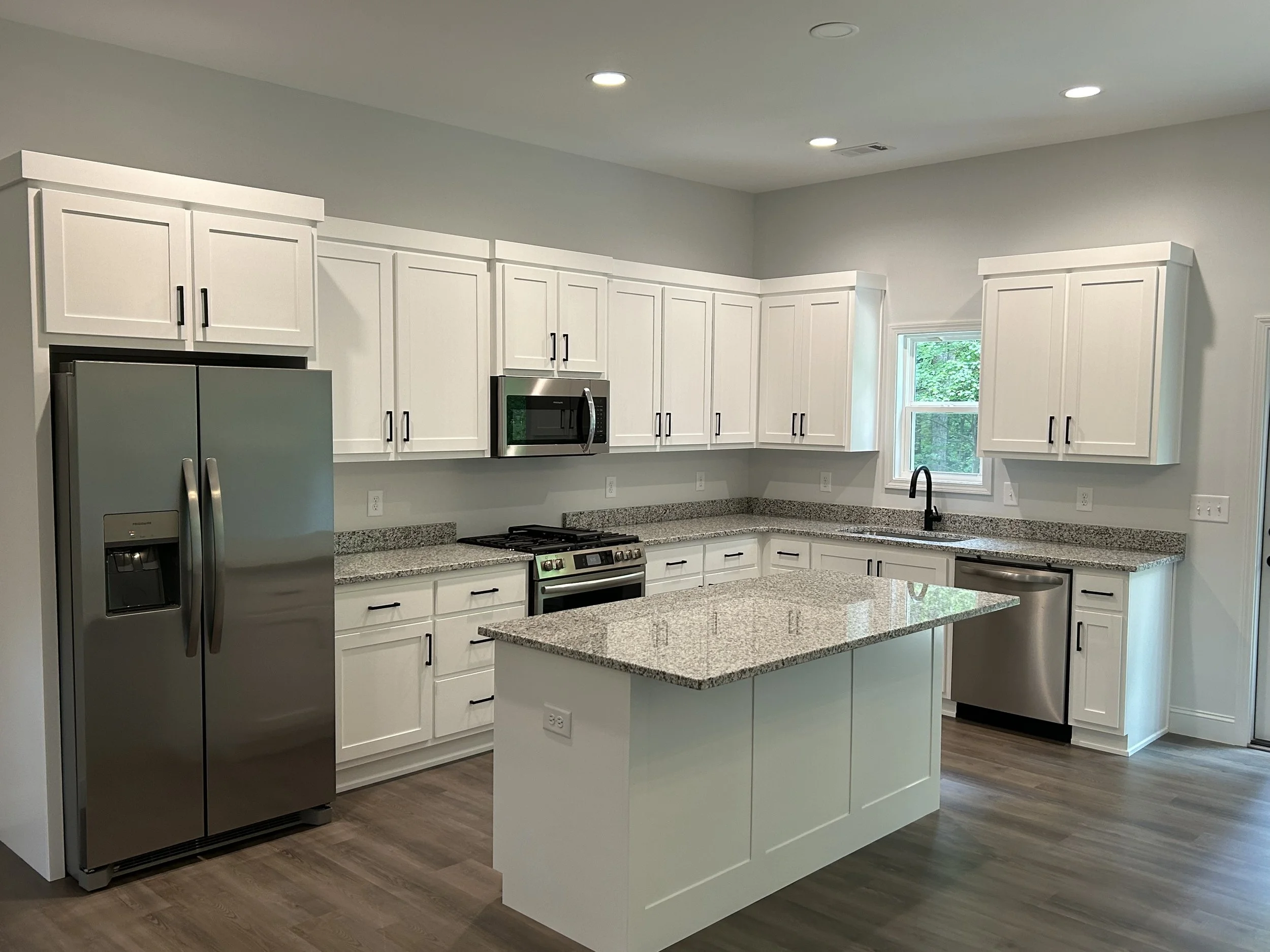 Modern kitchen with white cabinets, granite countertops, stainless steel appliances, and a small window above the sink.