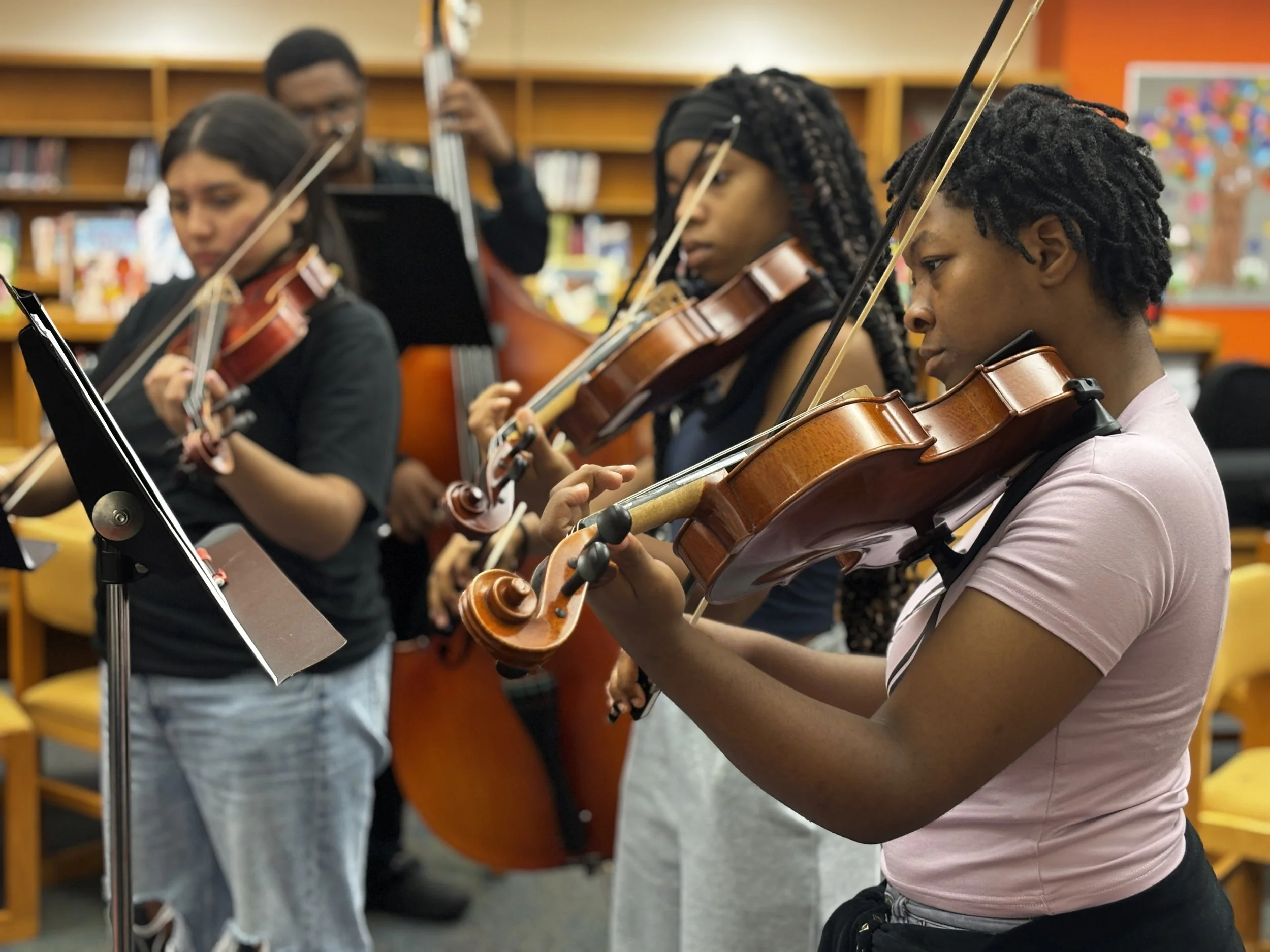 Group of young people playing violins in a music classroom.
