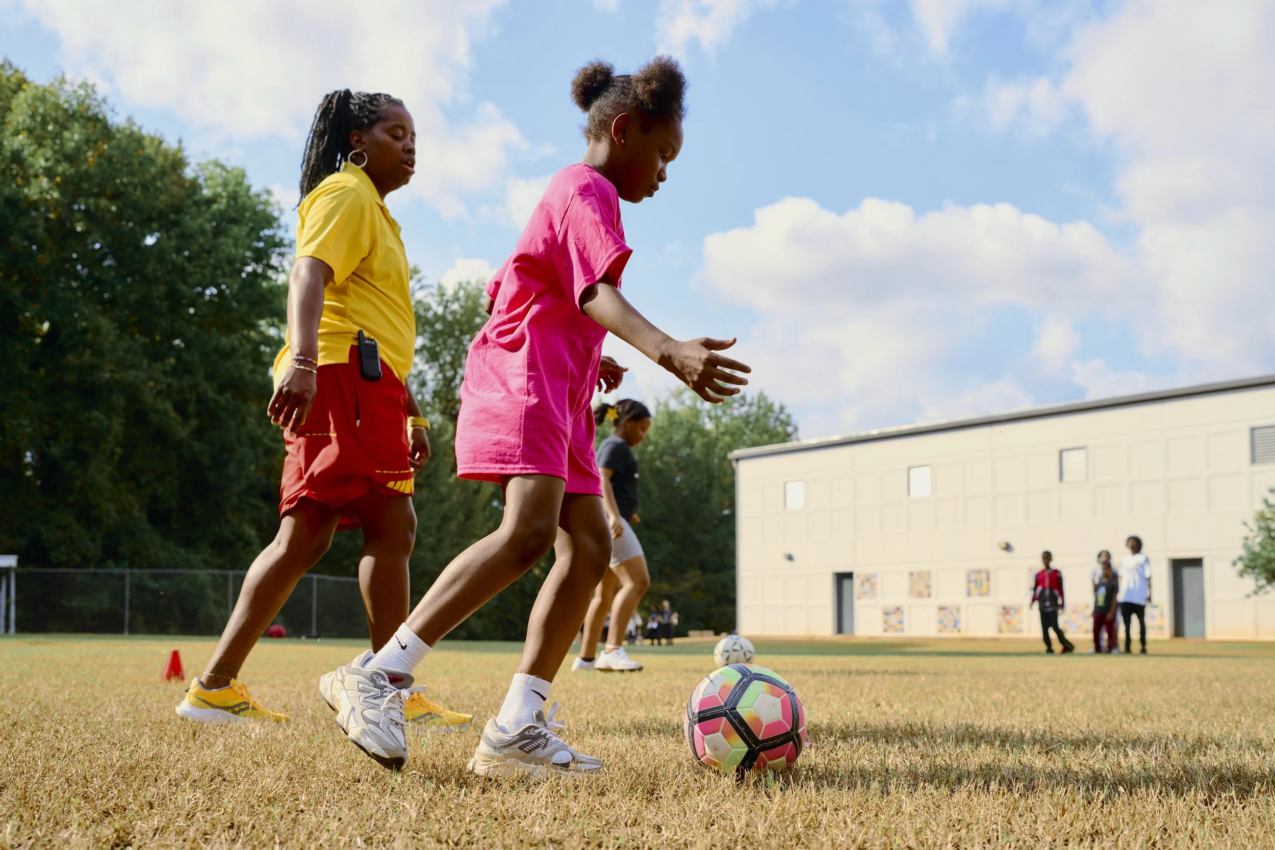 Children on a soccer field practicing with a colorful soccer ball on a sunny day.