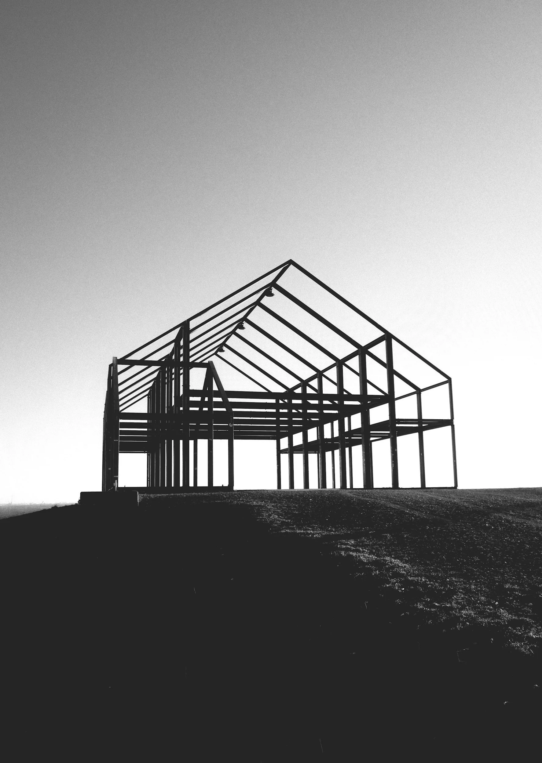 Black and white photo of an unfinished house frame on a hill under a clear sky.