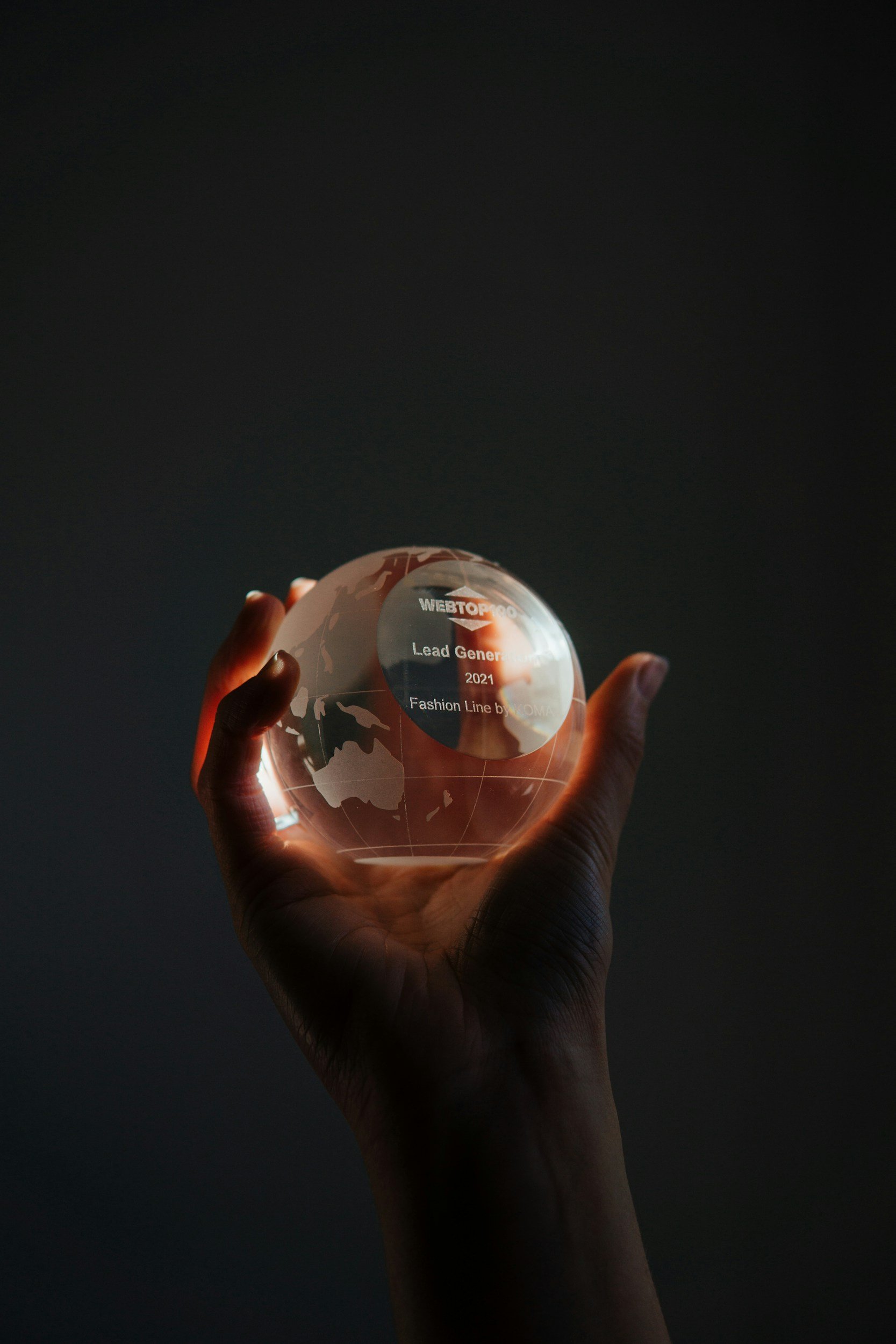 Hand holding a transparent glass globe with writing on it, against a dark background.