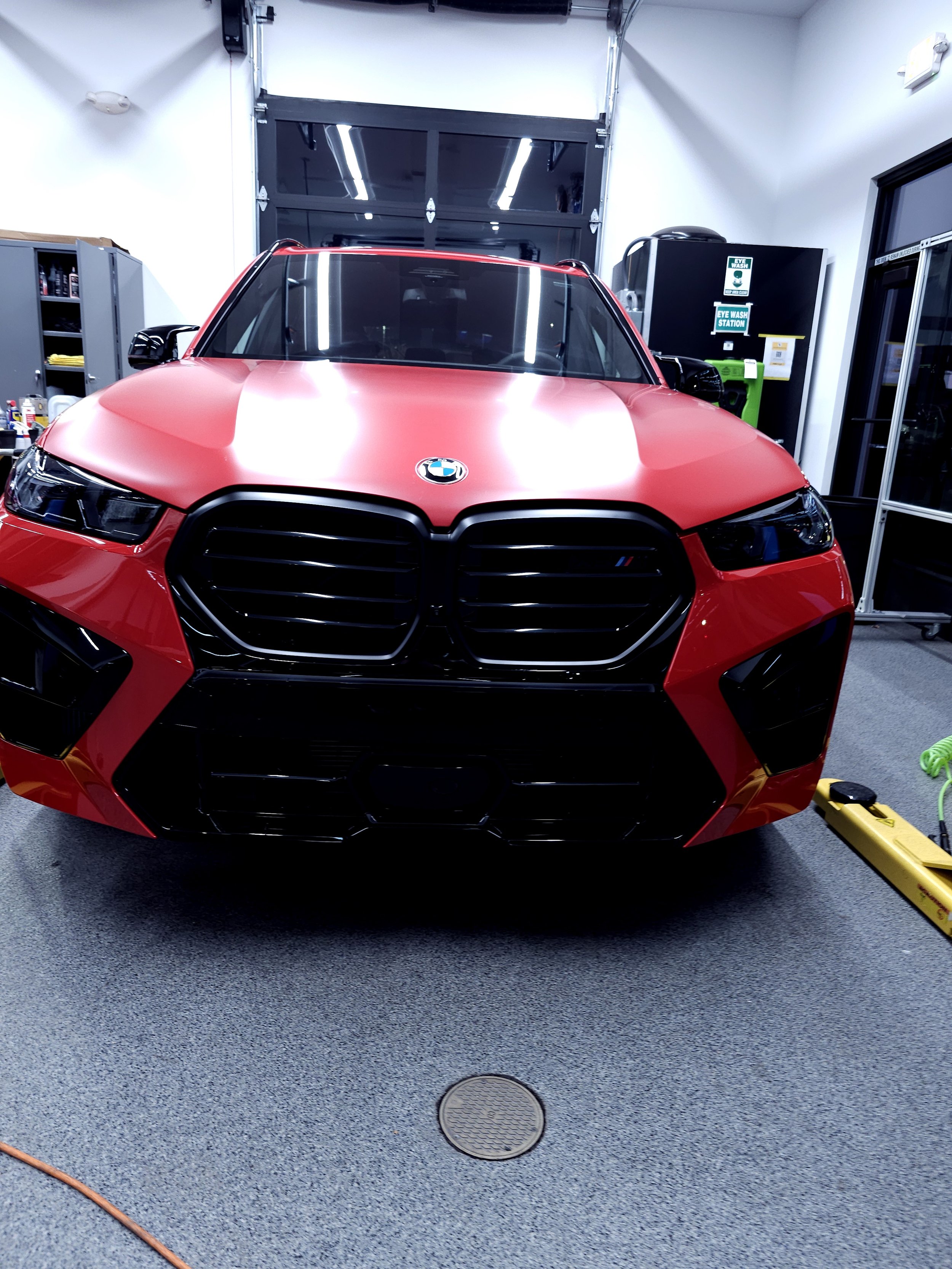 Front view of a red BMW car inside a garage or workshop, with black grille and BMW logo on the hood, surrounded by tools and equipment.