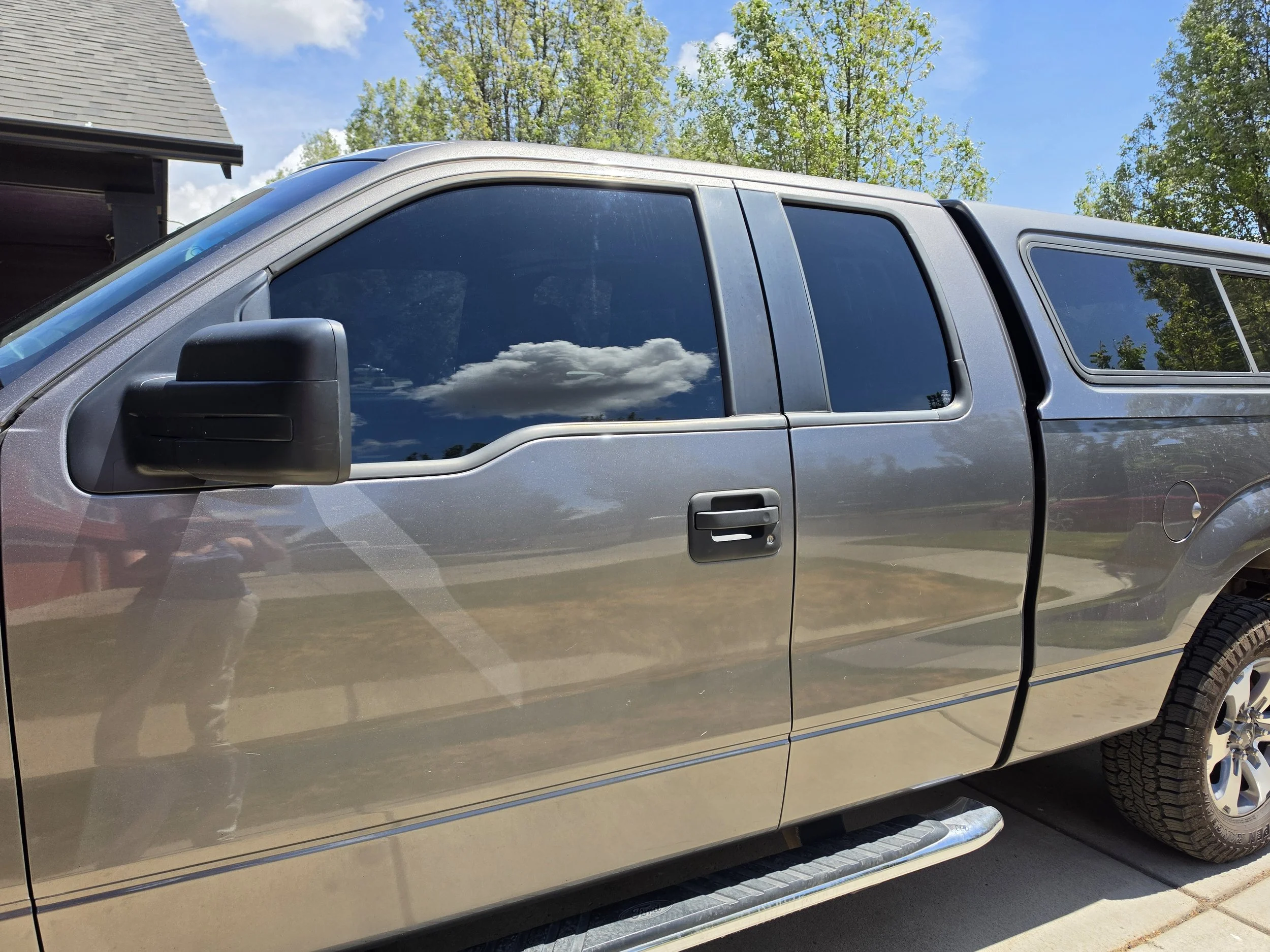 A silver pickup truck parked outdoors, reflecting the sky and trees in its windows.