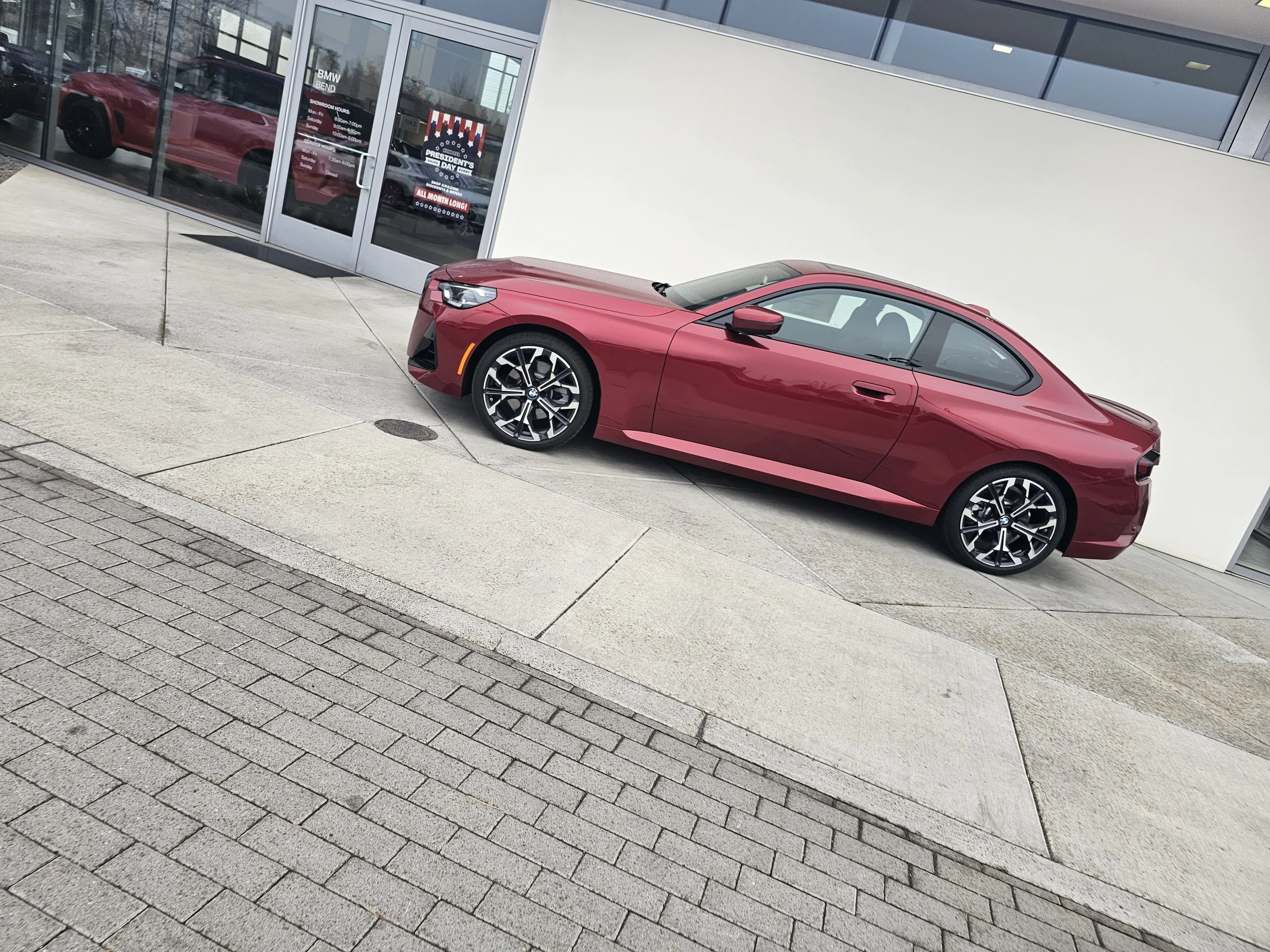 A red sports car parked outside a modern building with glass windows and a white exterior wall.