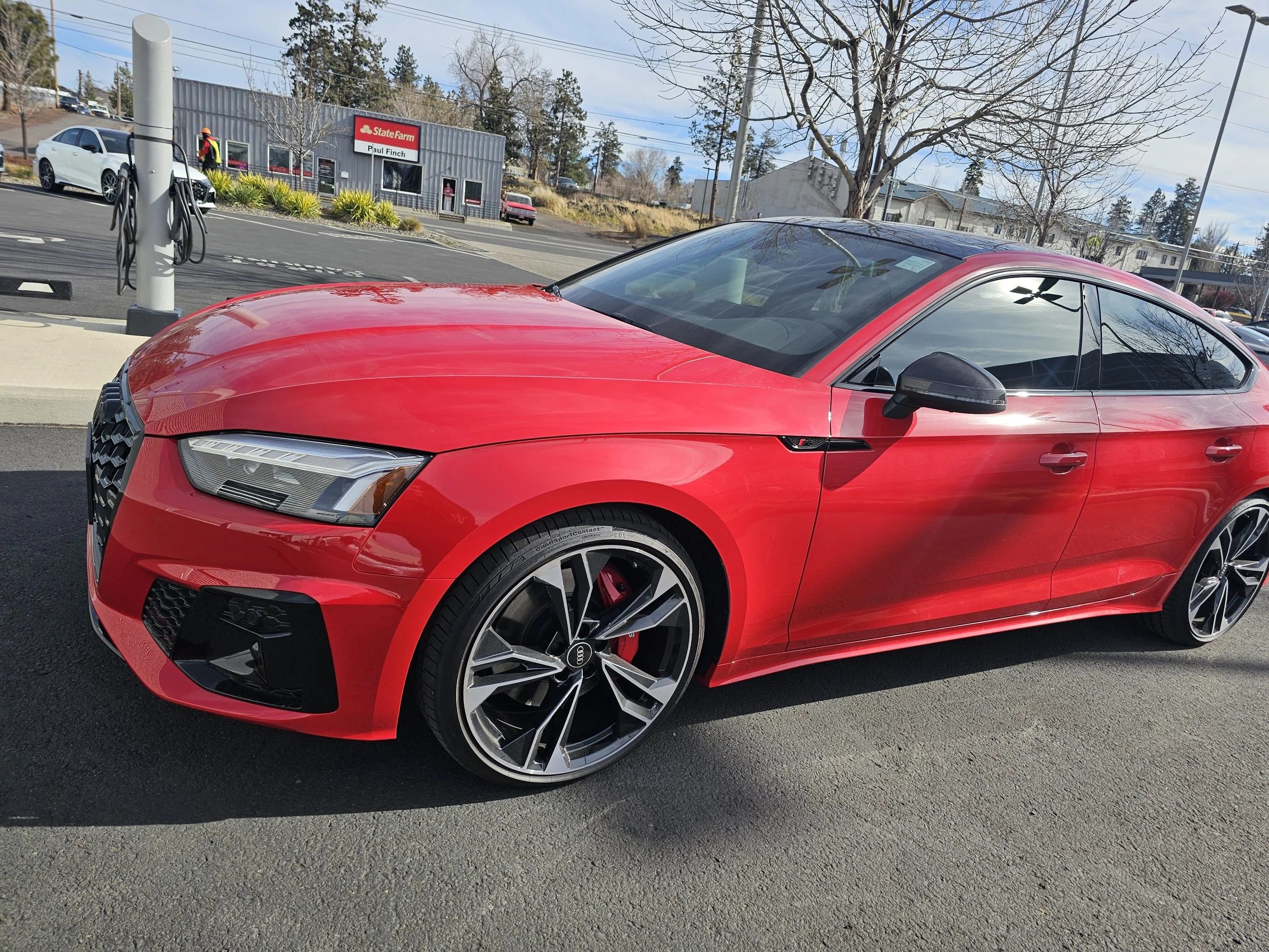 Red Audi sports car parked at a charging station with electric vehicle charger and charging cables in a parking lot.