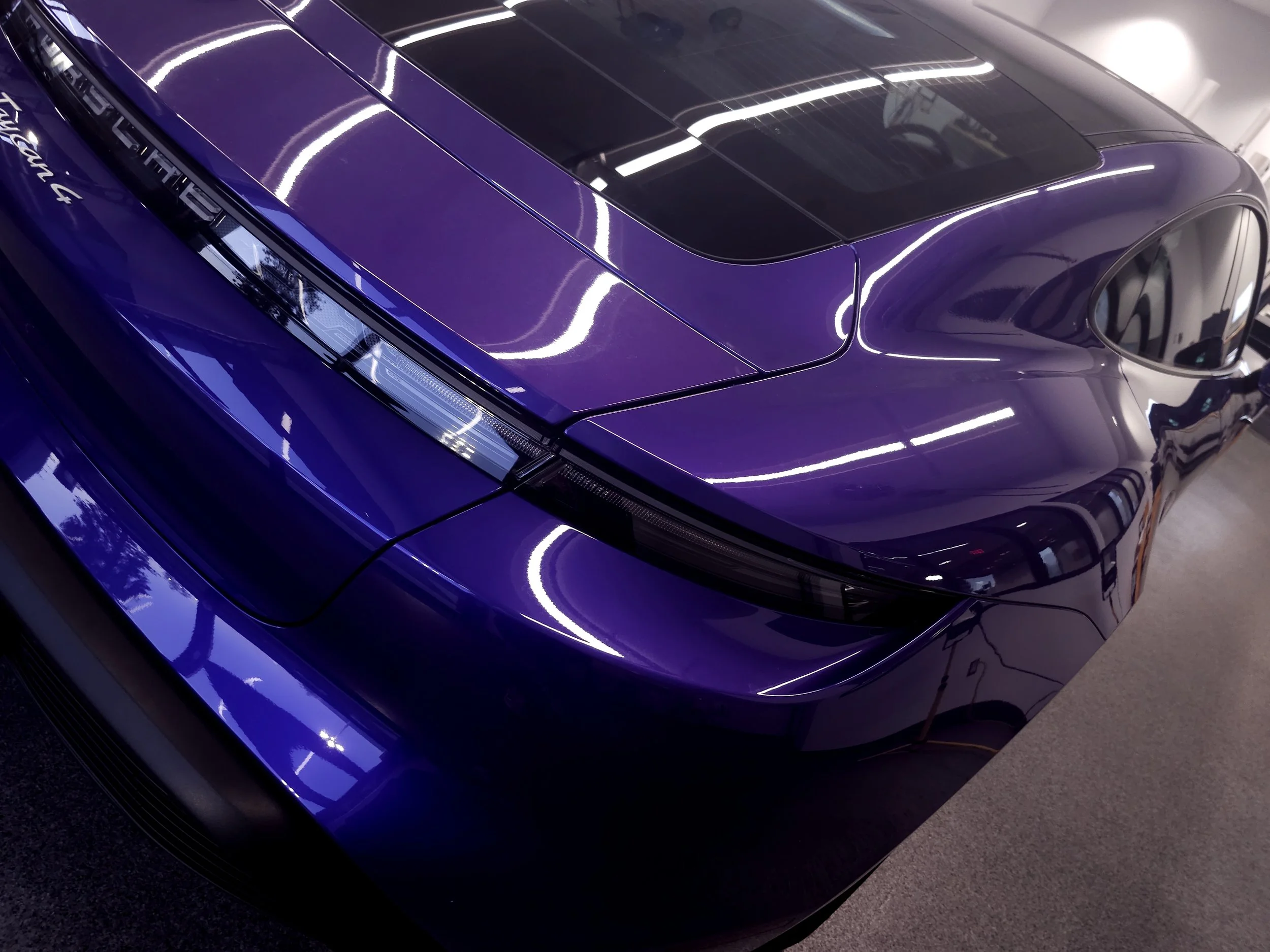 A purple sports car with a sleek design and a black roof panel, parked indoors under bright fluorescent lights.