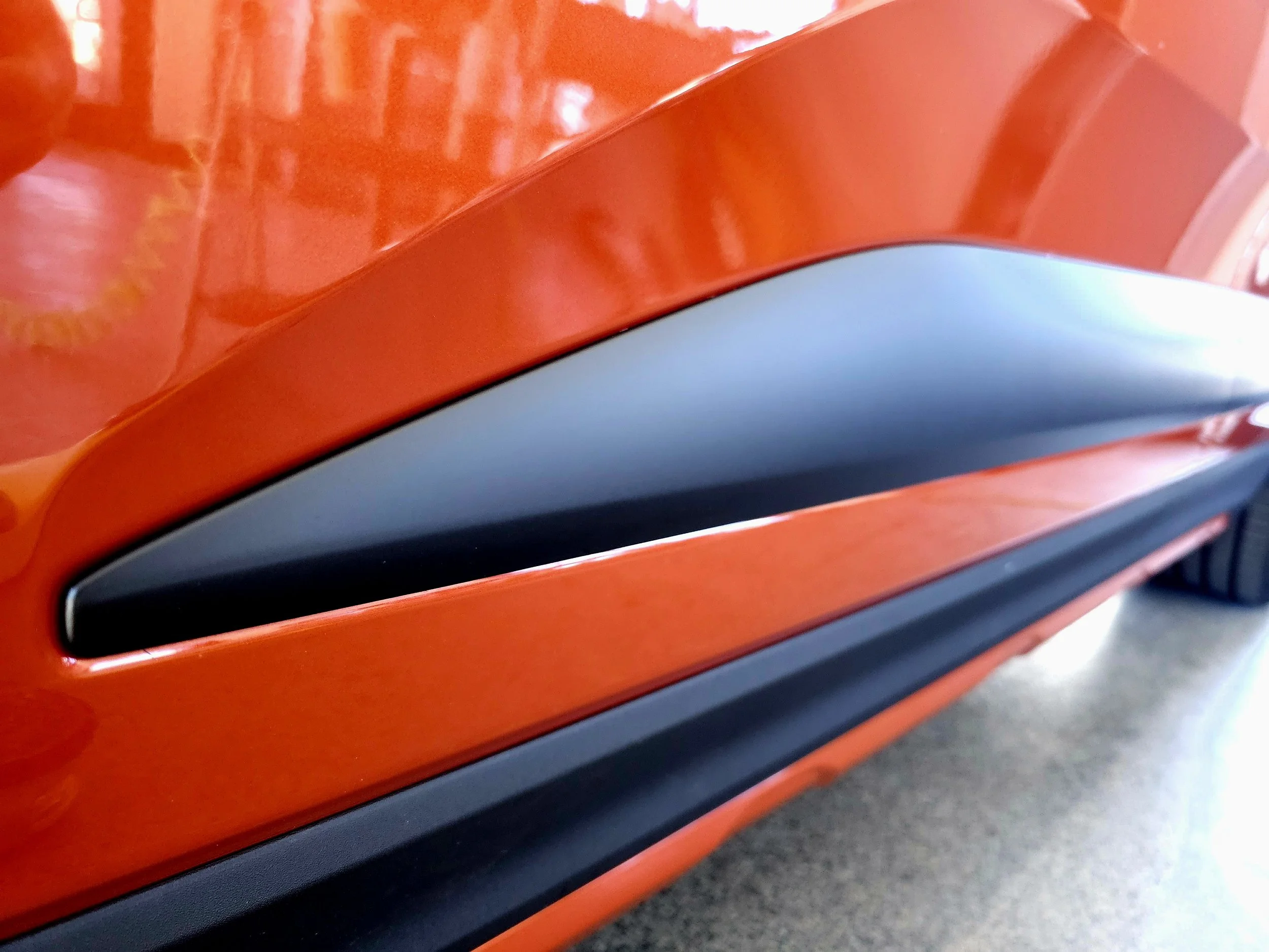 Close-up of a red and black object with smooth, reflective surfaces, showing a curved shape. The background appears to be a gray concrete floor.