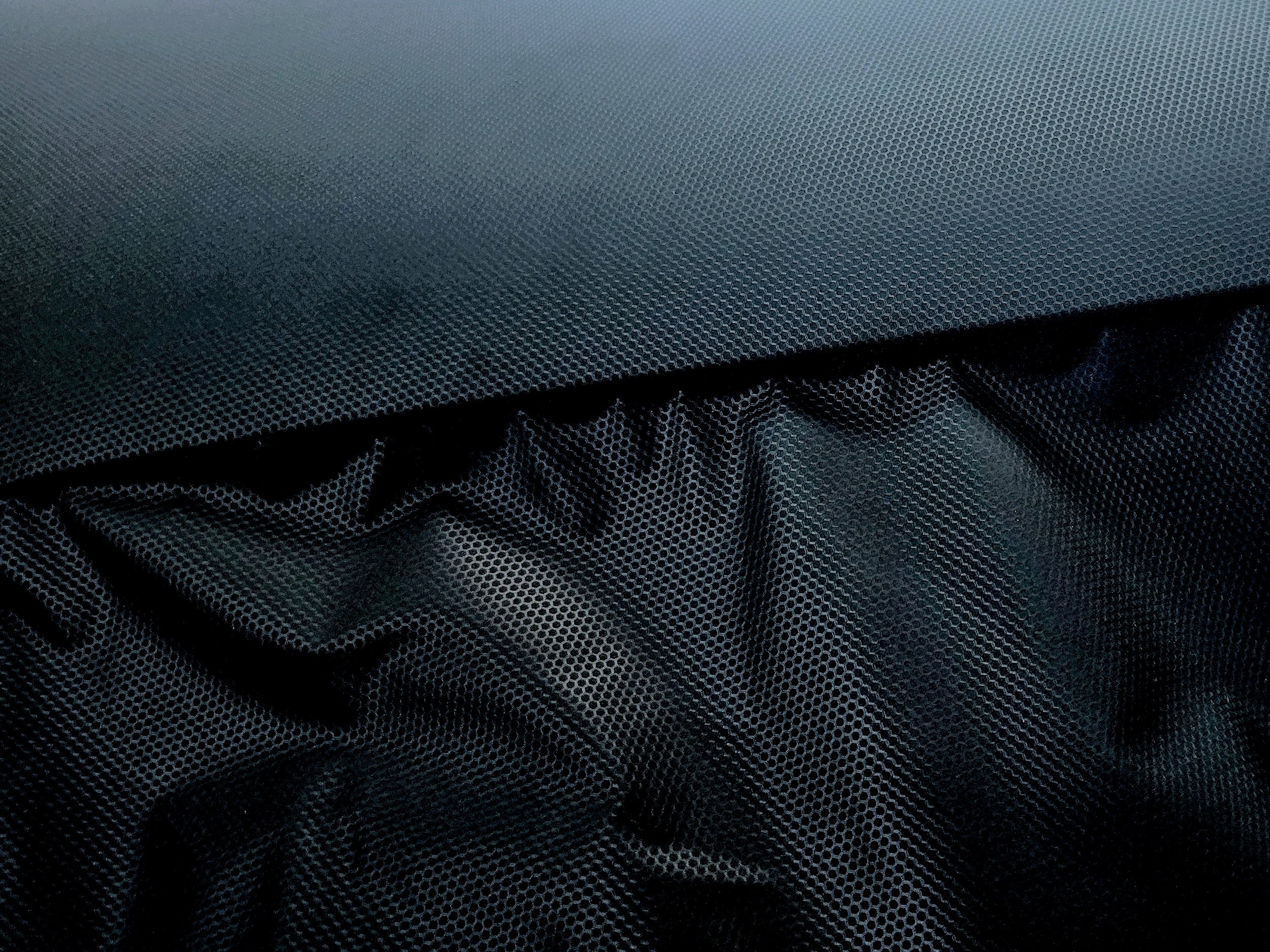 Close-up of textured black and gray fabric with a honeycomb pattern on the top and a darker, more textured fabric underneath.