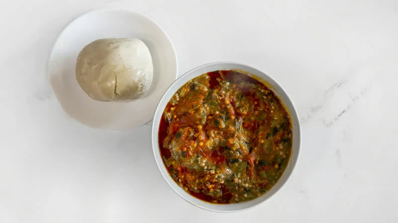 A bowl of vegetable stew and a ball of dough on a white surface