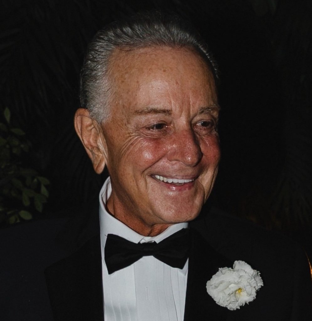 Barry J. Sawayer smiling in a tuxedo with a white shirt, black bow tie, and a white boutonnière, against a dark background.