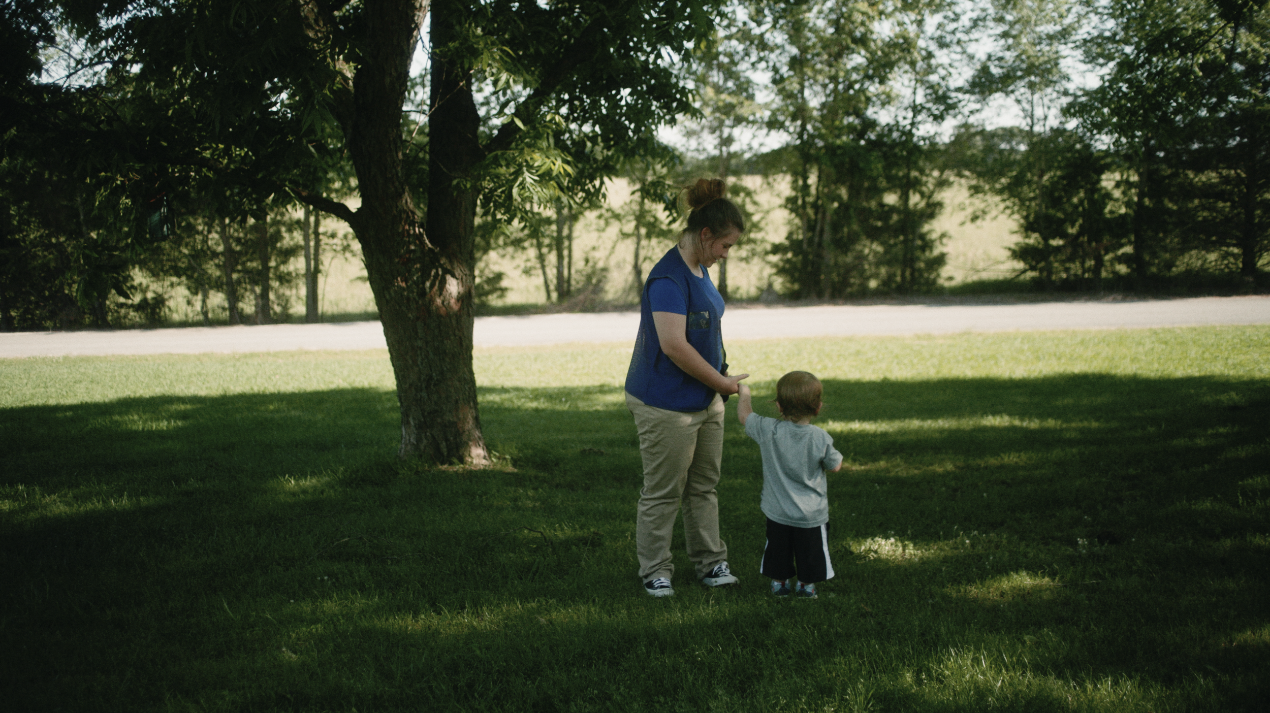 A woman and a young boy are standing on a grassy area under a tree.