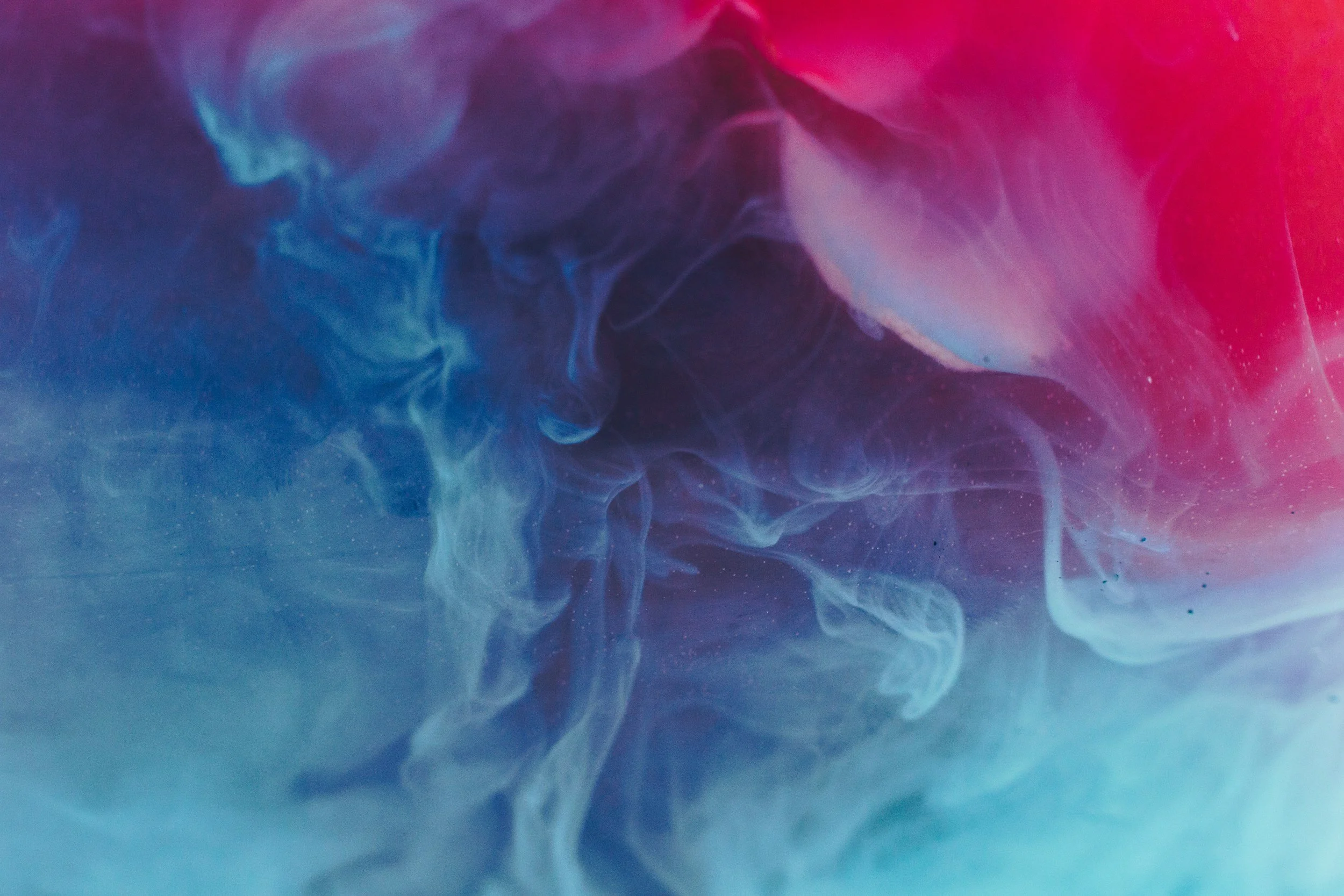 Colorful swirling smoke or ink in water with shades of blue, pink, purple, and hints of white.