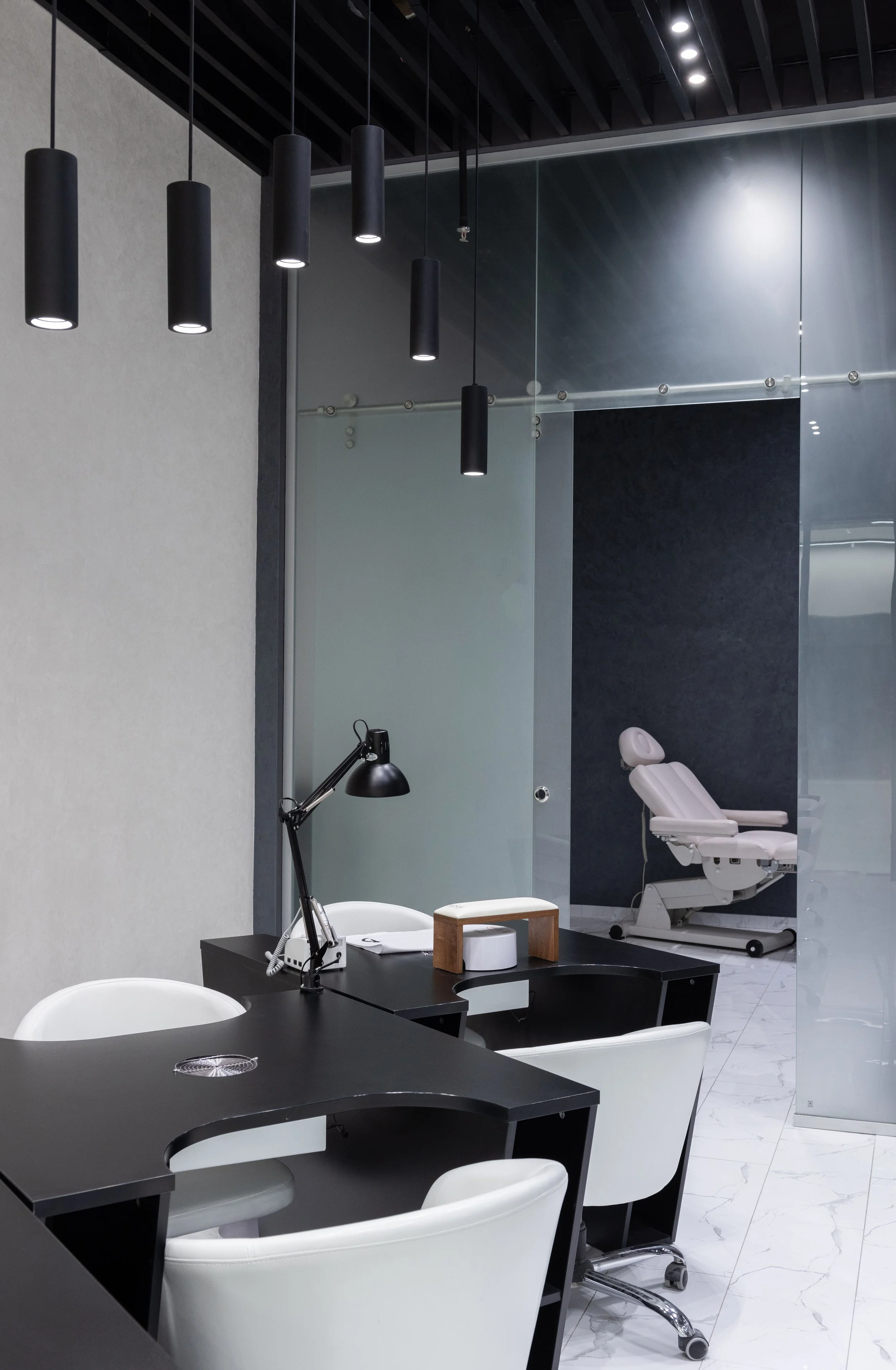 Modern dental office with a black desk, white chairs, a dental chair in the background, and sleek black pendant lights hanging from the ceiling.